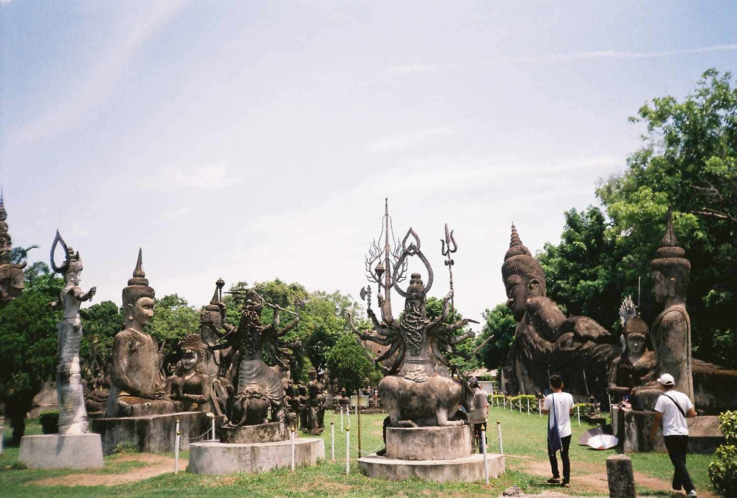 萬象市的驚人佛像公園 壁紙 — 一個寬敞的戶外雕塑公園，在明亮的天空下充滿了大型風化的神靈和神話人物雕像。
