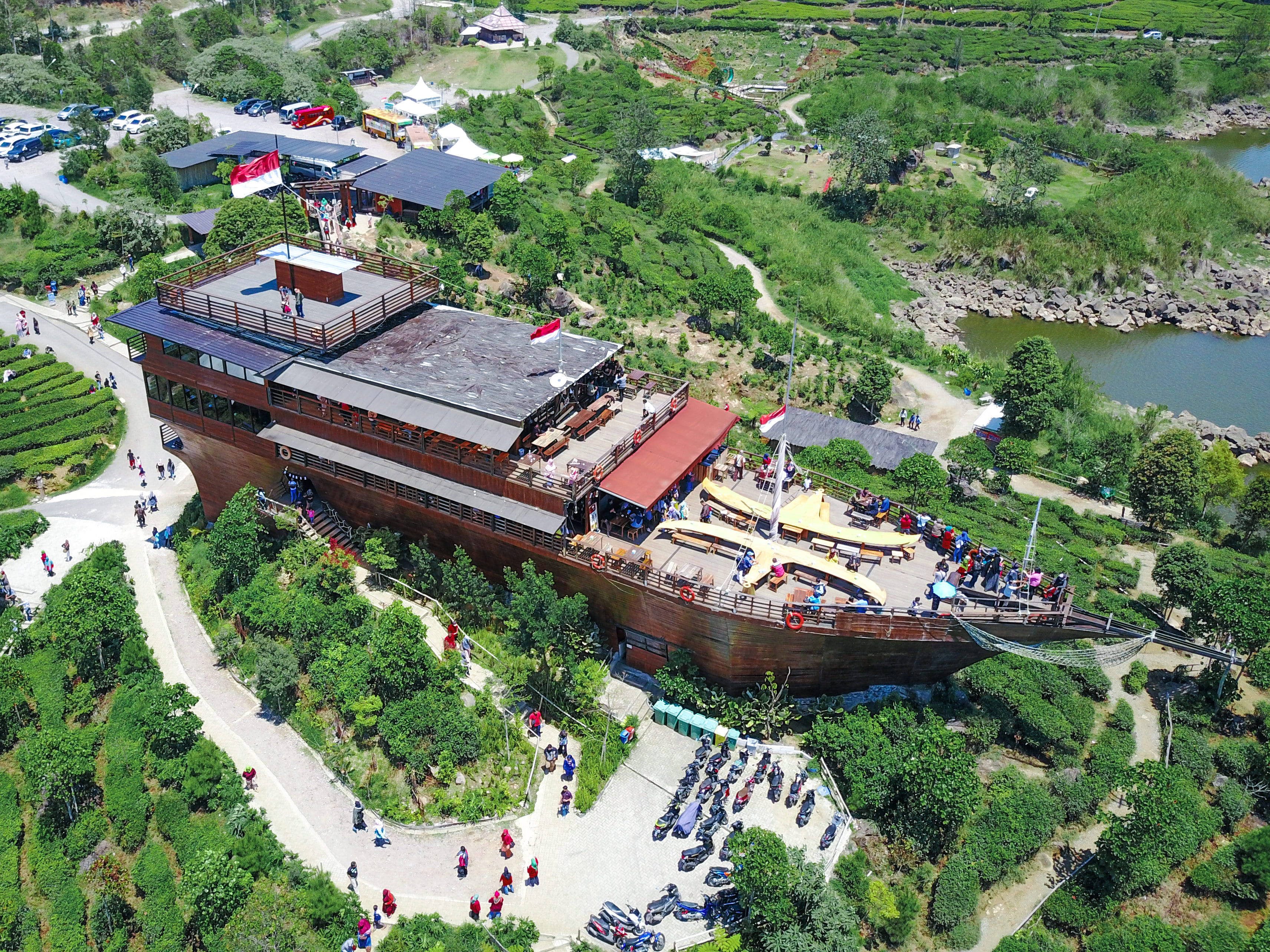 萬隆帕滕甘格露營地與餐廳 壁紙 — 俯瞰一座巨大的木造船形建築，坐落在鬱鬱蔥蔥的綠色茶園梯田中，遊客正在探索其甲板和周圍的小徑。