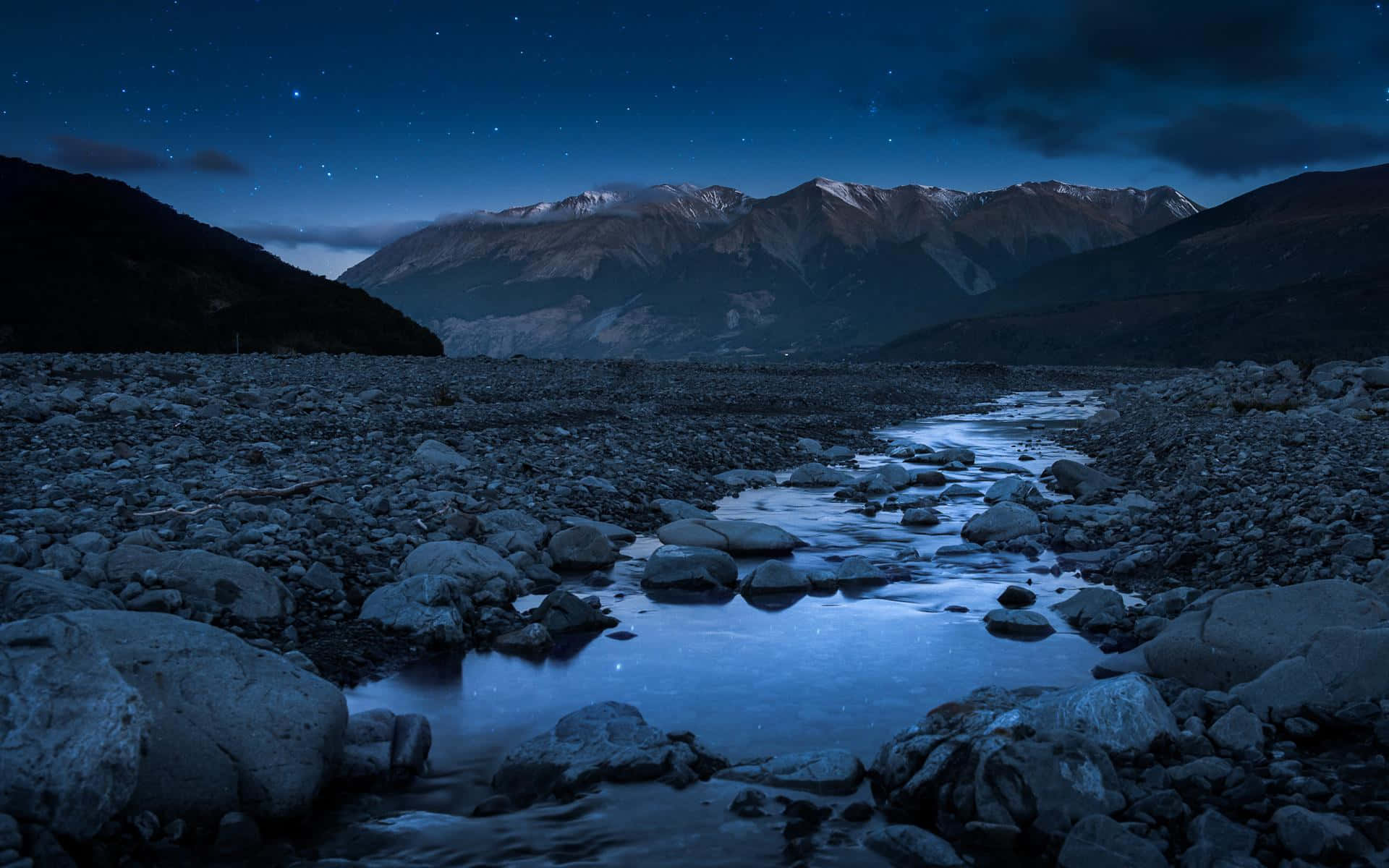 星空倒映在一條平靜的河流中，河流流經一個岩石山谷，有積雪覆蓋的山峰。