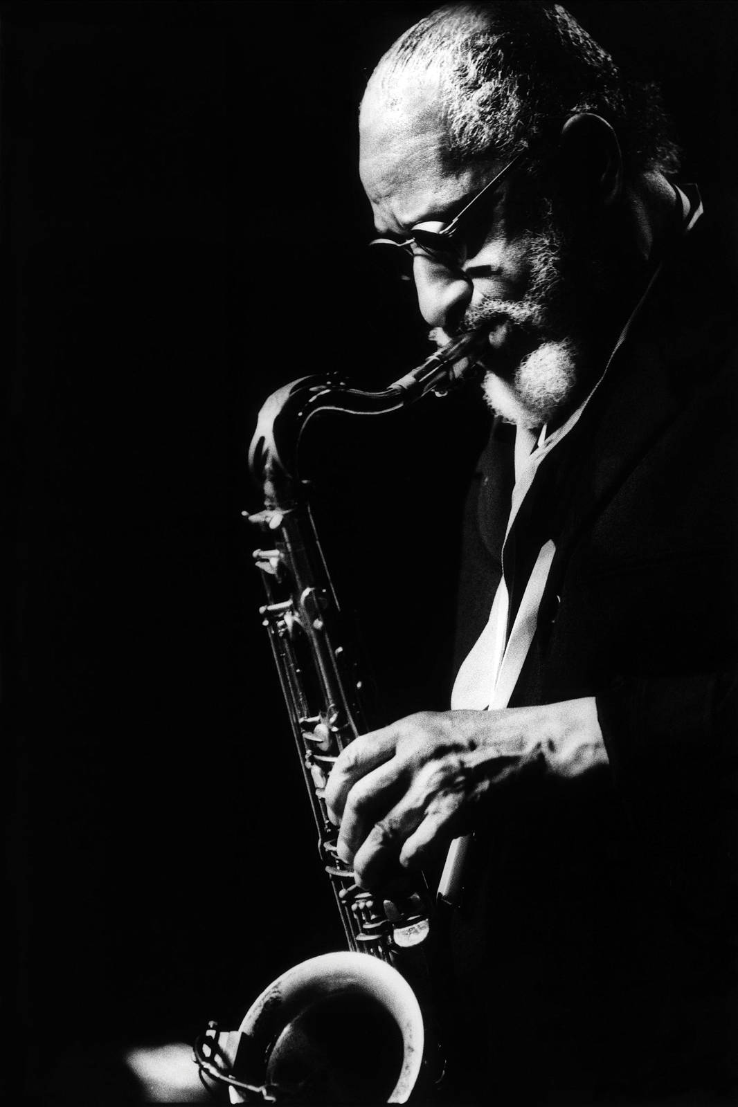 著名音樂家 Sonny Rollins 的美學肖像 壁紙 — 一位爵士薩克斯風手側面演奏樂器，在黑色背景下的戲劇性聚光燈下。