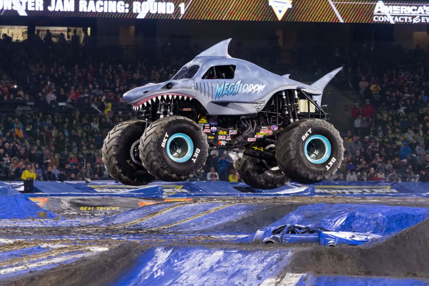 著名鯊魚怪物卡車 壁紙 — 一輛名為 Megalodon 的鯊魚主題怪獸卡車在 Monster Jam 活動期間，在擠滿人的室內競技場中飛越藍色坡道。