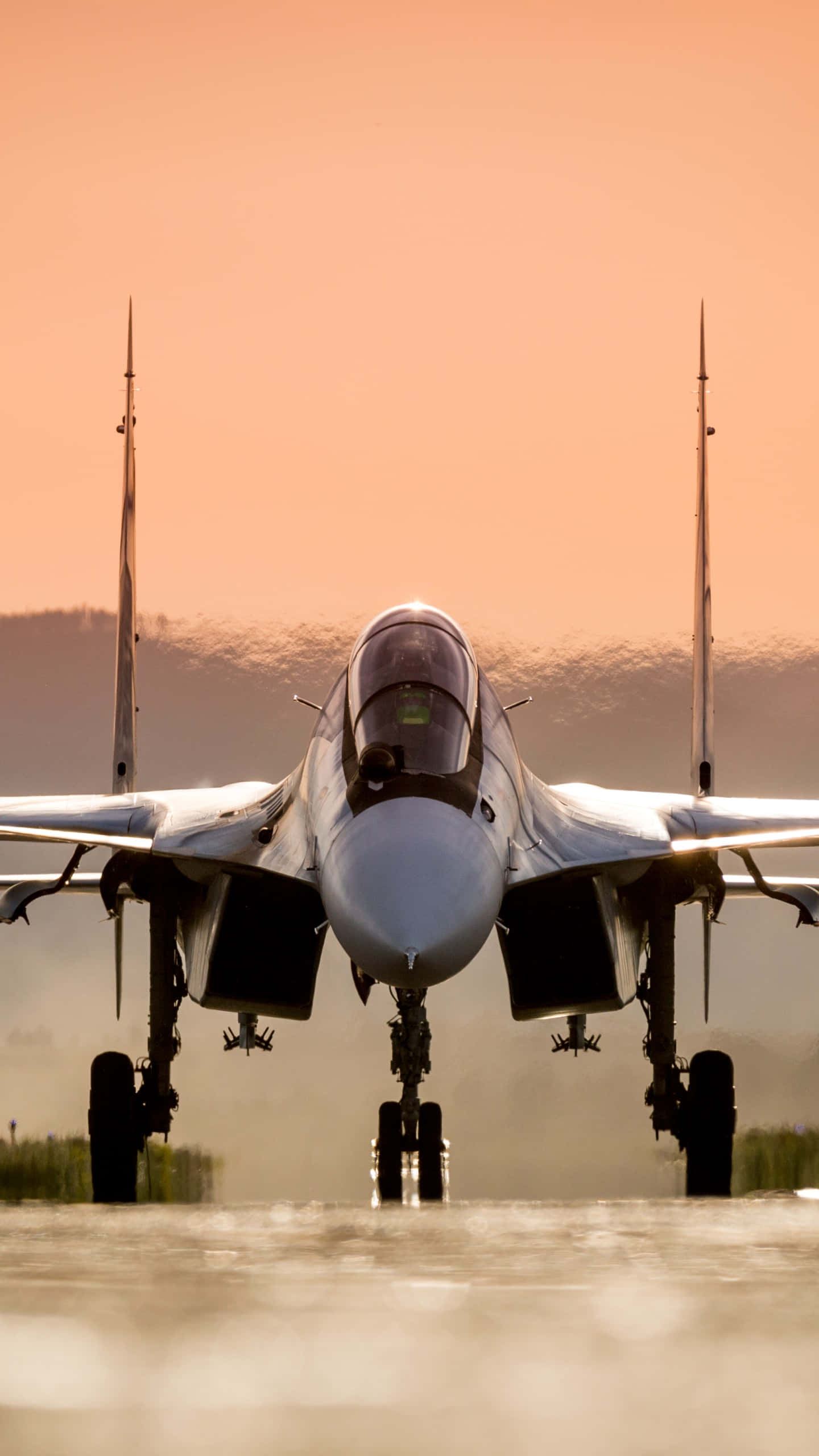 著陸中的蘇霍伊Su-30 Android巨無霸飛機背景 壁紙 — 一架戰鬥機在跑道上向前，夕陽西下，溫暖的橙色天空和遠處的山丘。