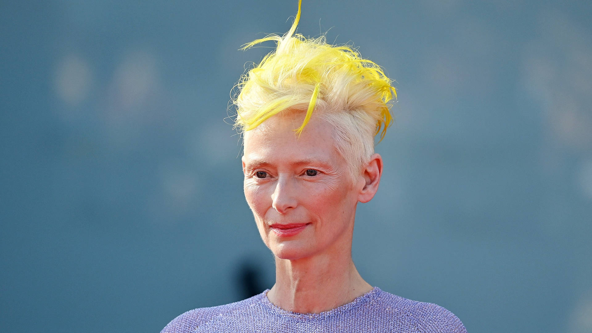 蒂達·史雲頓（Tilda Swinton）留著亮黃色尖刺髮型，身穿紫色上衣。