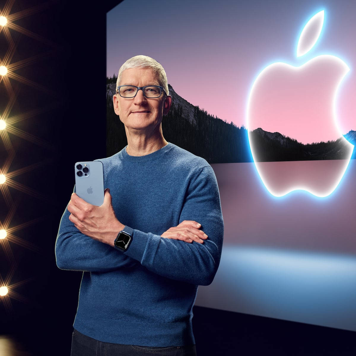 Tim Cook 在山景日落背景前，手持 iPhone 站在發光的 Apple 標誌前。