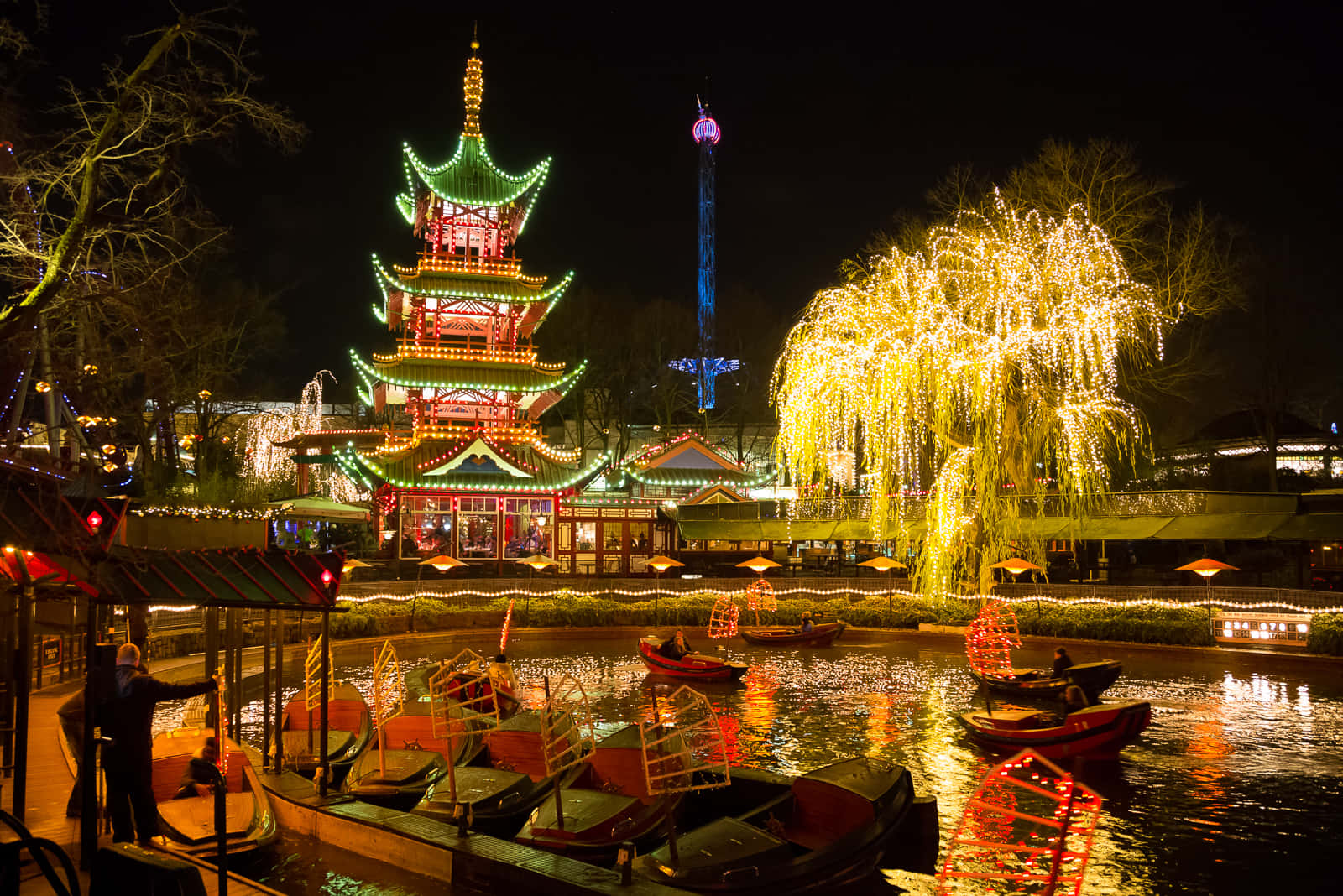 蒂沃利花園夜間璀璨的中式塔樓 壁紙 — 節日遊樂園的充滿活力的夜景，有發光的寶塔、照亮的柳樹和反射運河上的船隻。
