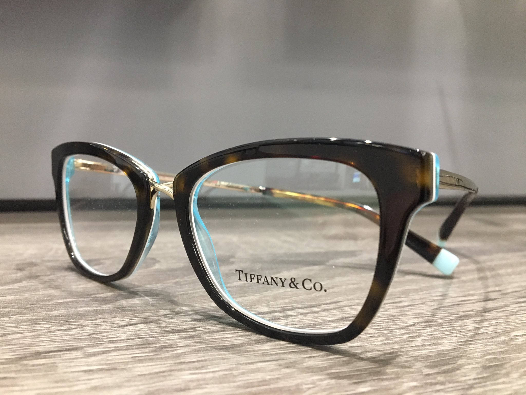 蒂芙尼 TF2186 長方形眼鏡 壁紙 — 優雅的玳瑁色Tiffany & Co.眼鏡，帶有淺藍色點綴，放置在木質表面上。