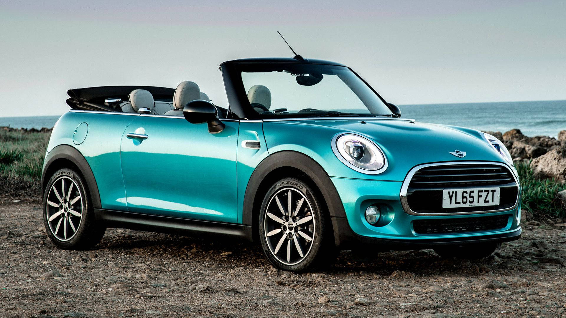 綠松色MINI Cooper開篷車停泊在近海的岩石海灘上。