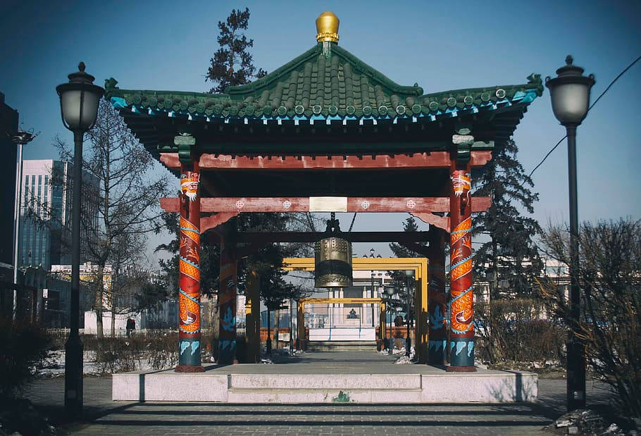 蒙古寺廟中的大鐘 壁紙 — 一座傳統裝飾性亭子，帶有龍紋柱子和綠色瓦頂，矗立在白雪覆蓋的城市公園中，天空清澈湛藍。
