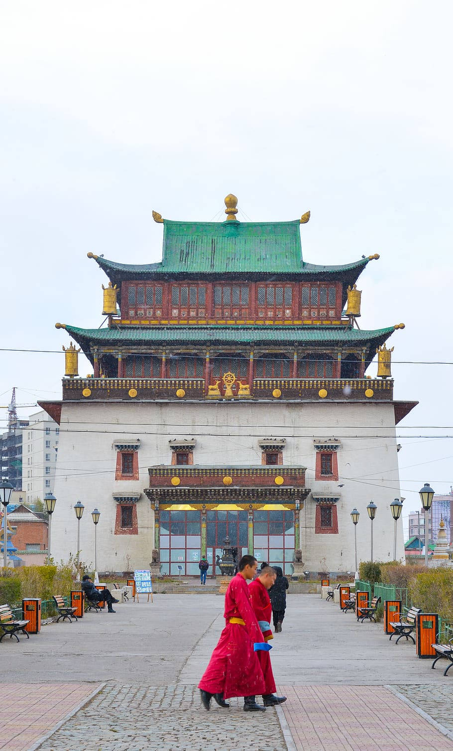 蒙古甘丹泰金倫寺莊嚴風景 壁紙 — 兩位身穿鮮紅色長袍的僧侶，在陰天之下走過一座宏偉的傳統蒙古寺廟，寺廟有綠色屋頂和金色裝飾。