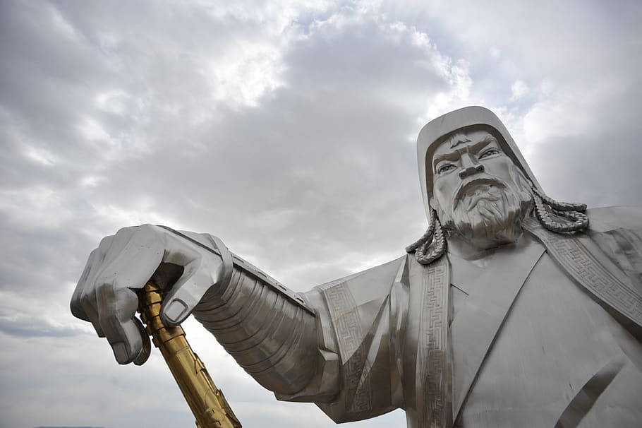 蒙古鐵木真雕像 壁紙 — 一座高聳的金屬成吉思汗雕像，手持金色權杖，背景是戲劇性的多雲天空。
