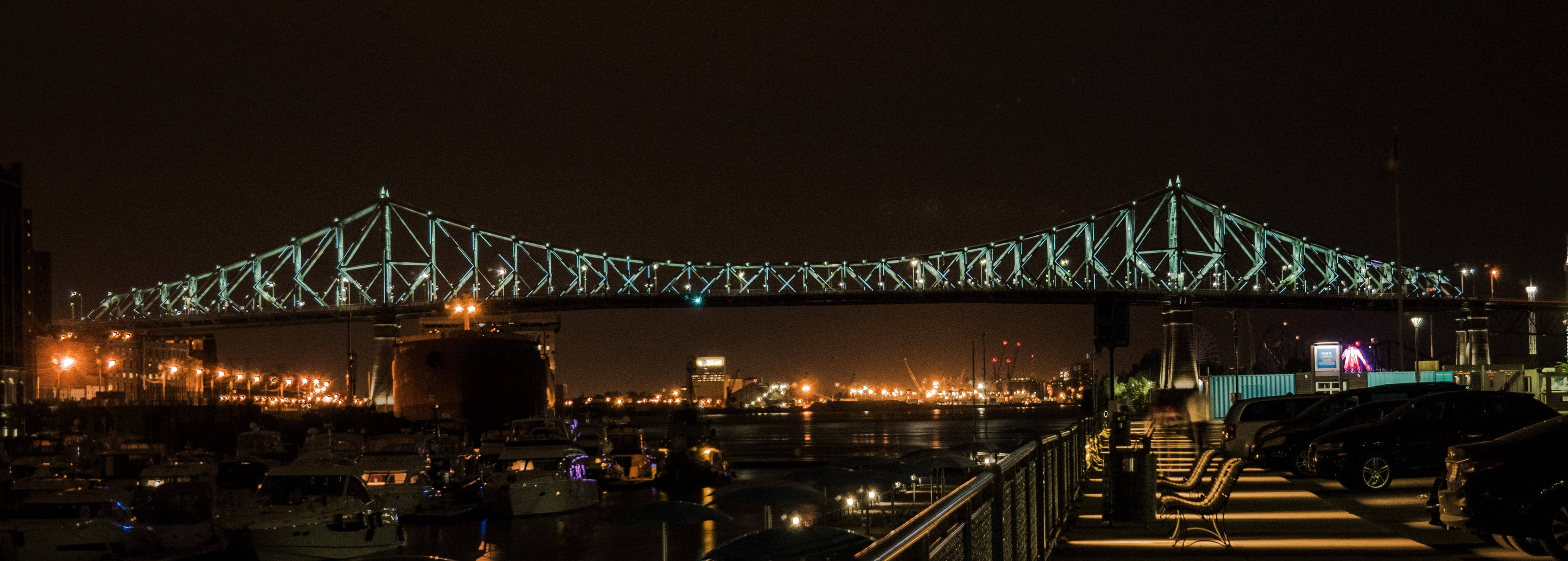 蒙特利爾雅克·卡地亞大橋 壁紙 — 令人驚嘆的夜景，一座亮燈的鋼桁架橋橫跨港口，船隻和城市燈光倒映在水面上。