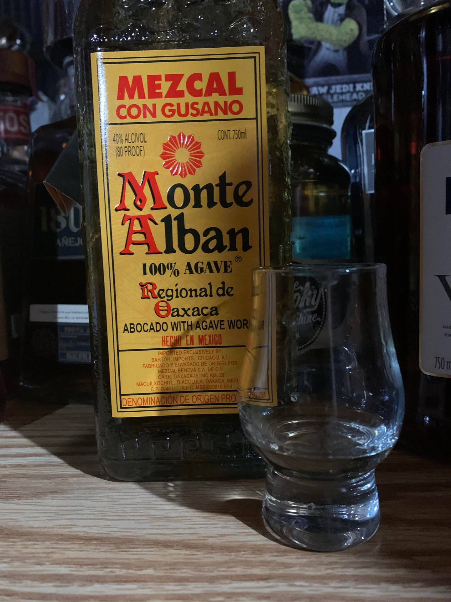 一瓶帶有gusano的Monte Alban梅斯卡爾酒和一個空的品酒杯放在木製吧檯上。