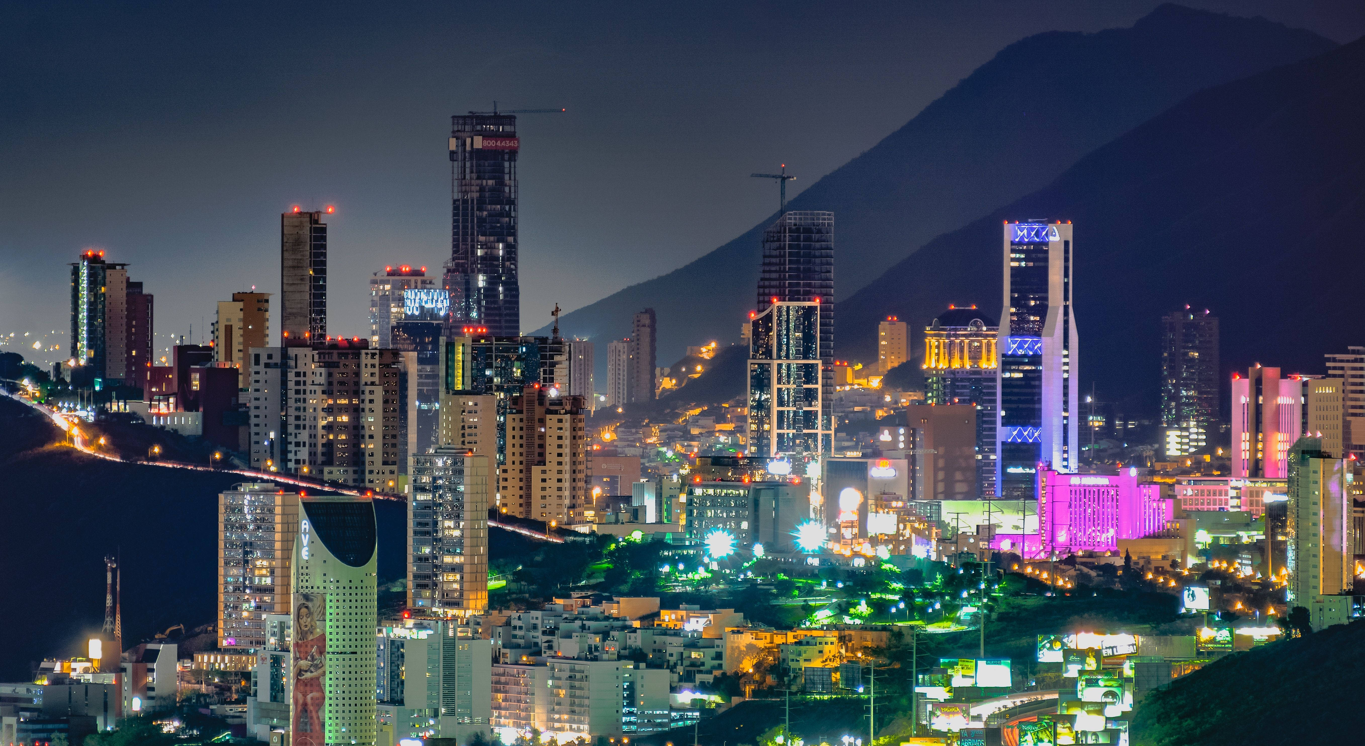 蒙特雷夜景城市風光 壁紙 — 夜晚充滿活力的城市景觀，有燈火通明的摩天大樓和背景中的山脈。
