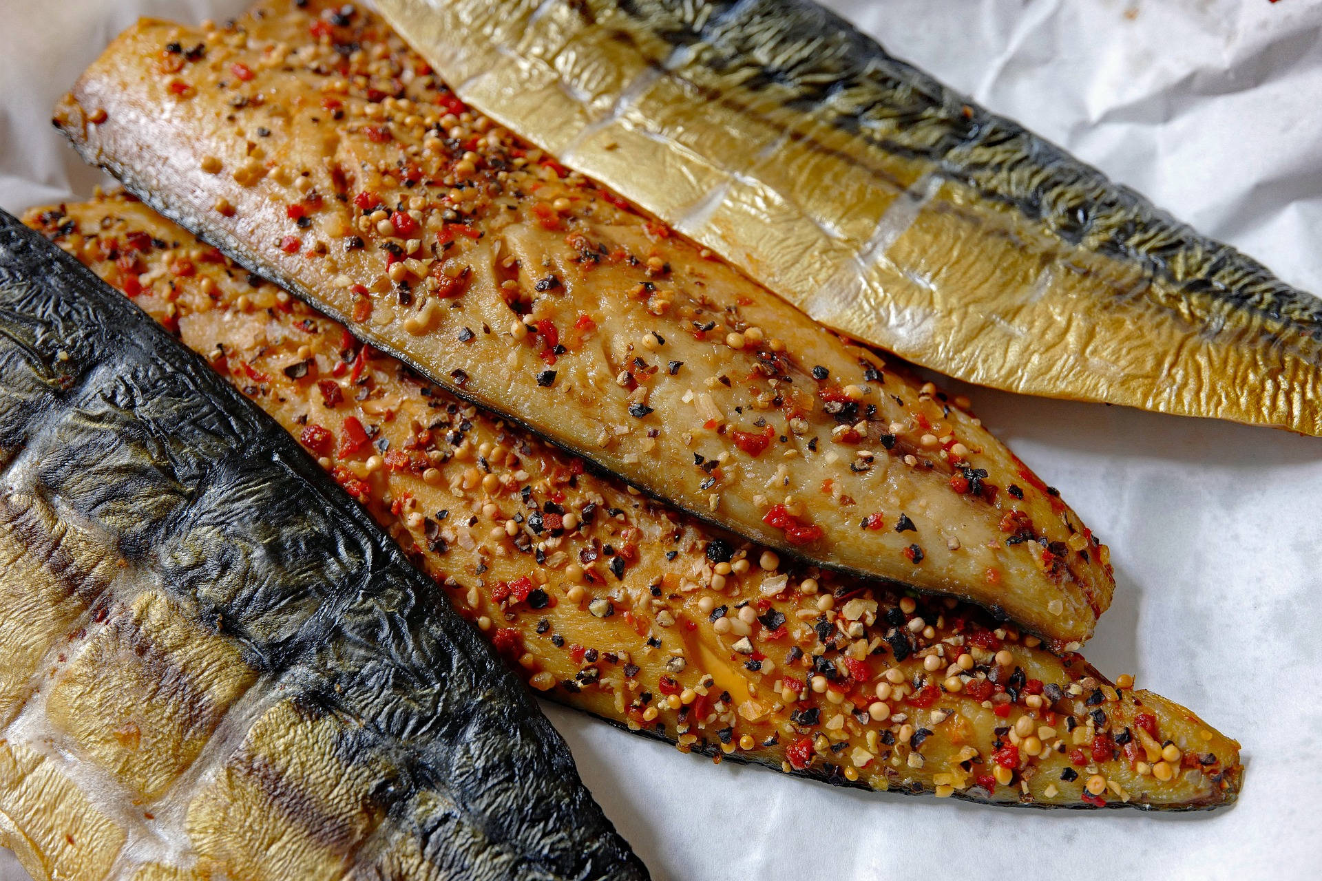 蒜香鰹魚魚排 壁紙 — 三塊烤鯖魚柳，上面撒上紅辣椒片和芝麻，放在皺巴巴的烘焙紙上。
