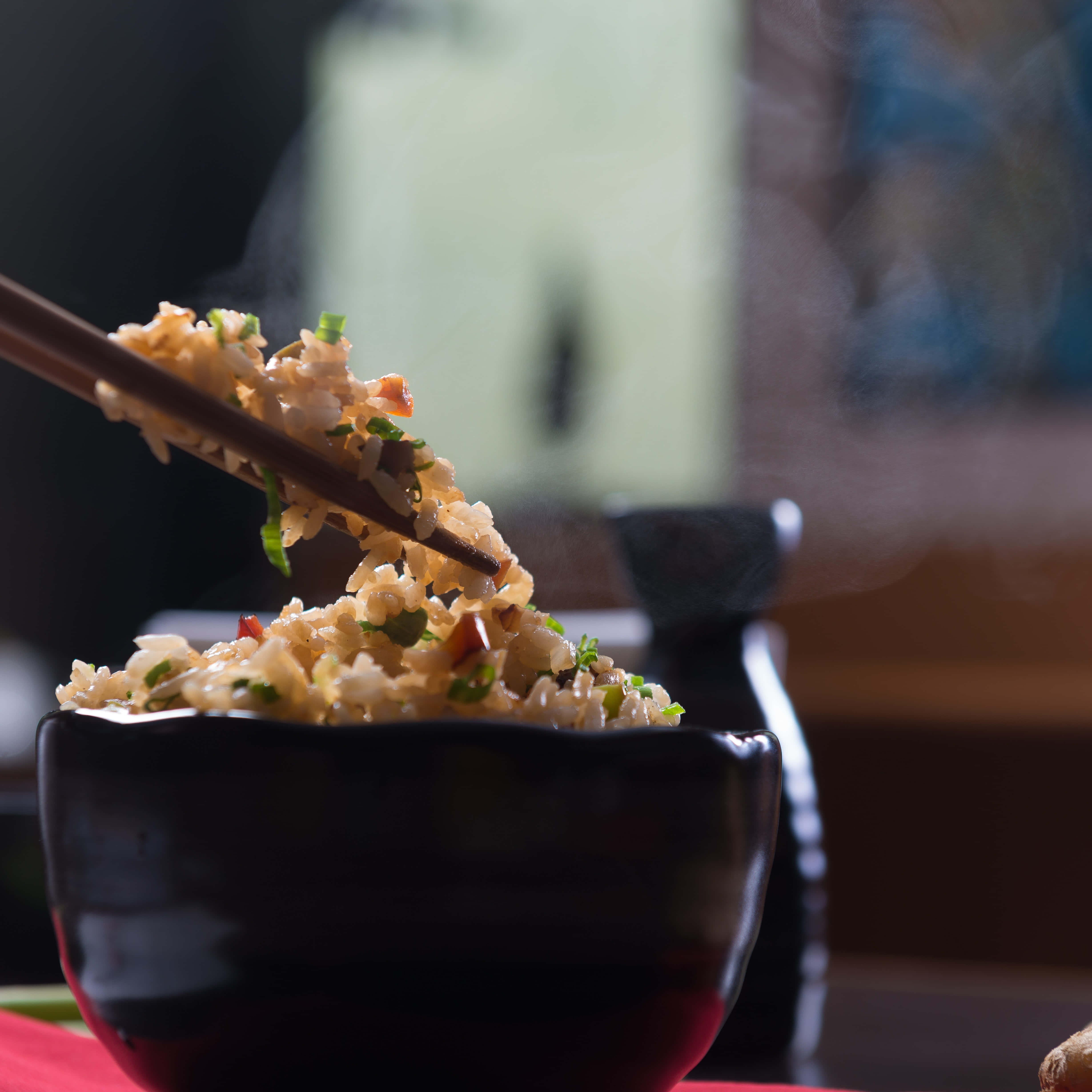 Rice 桌布 壁紙 — 蒸氣從一個黑色碗中的美味米飯升起，筷子夾起一口香氣撲鼻的飯粒朝向鏡頭。