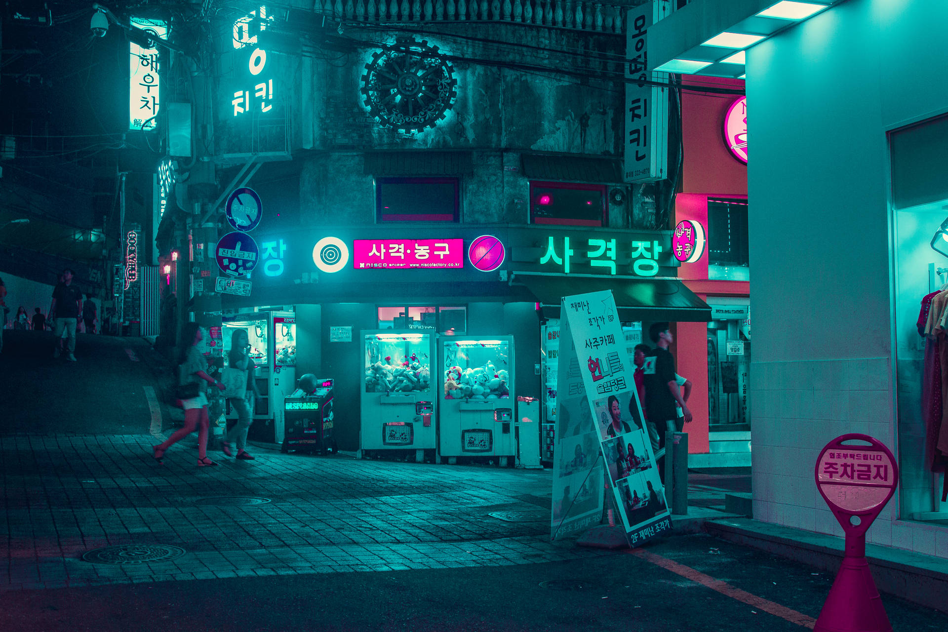 韓國夜晚的街道，有霓虹燈招牌、夾公仔機和行人。