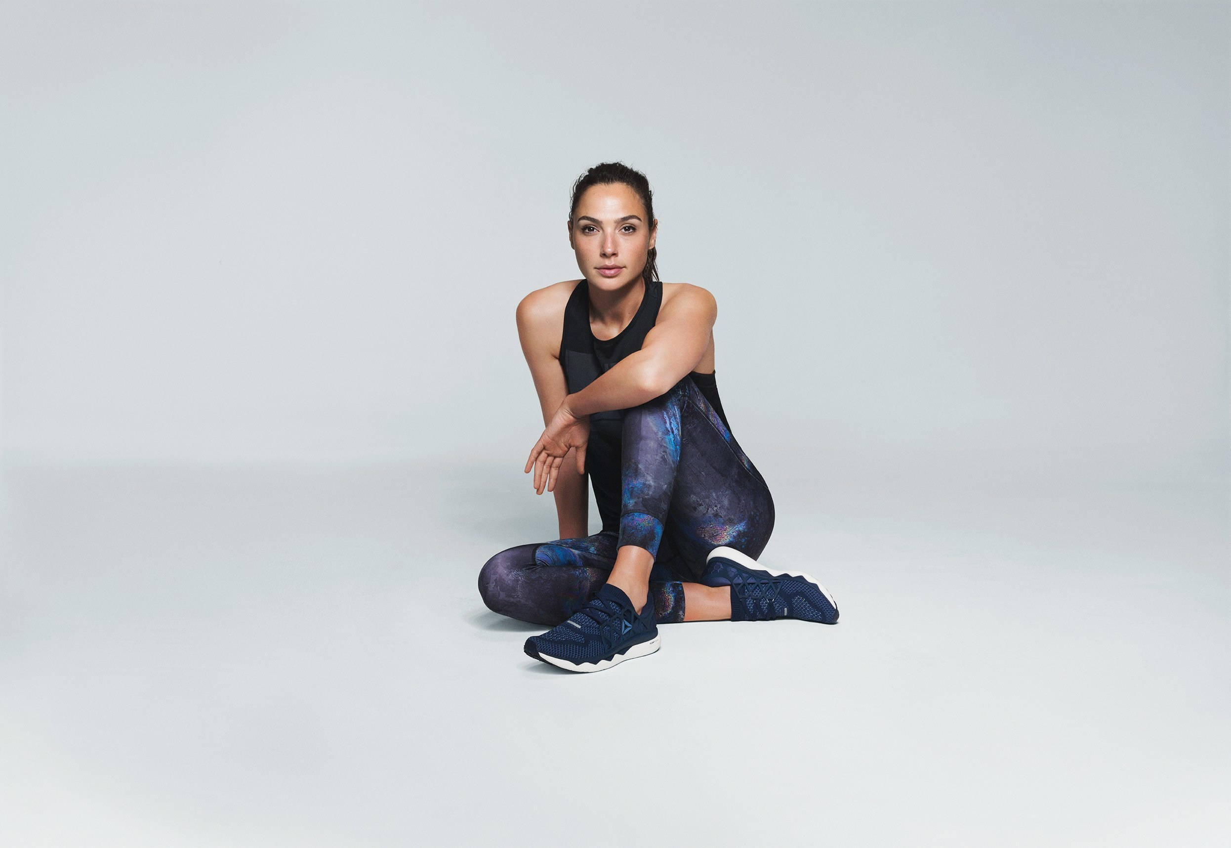蓋兒·加朵為Reebok代言 壁紙 — 一位穿著運動服的女性在無縫工作室背景的白色地板上端坐。