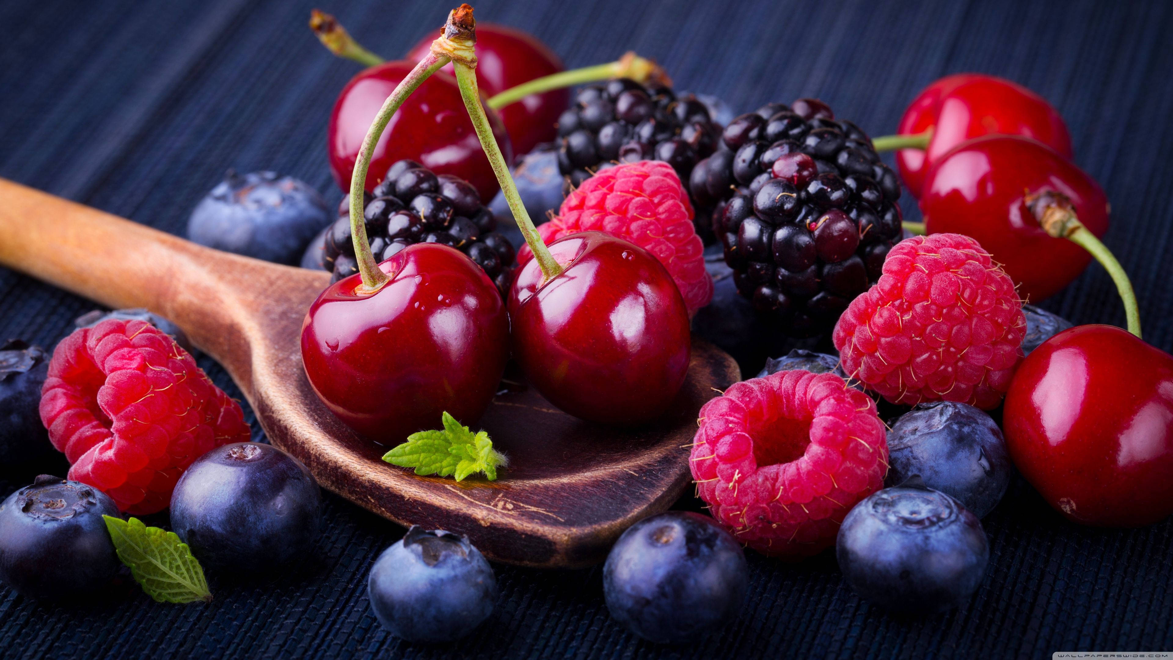 蔓越莓混合漿果一勺 壁紙 — 多汁的車厘子、紅桑子、黑莓和藍莓在木匙上閃閃發光，背景為深色紋理。