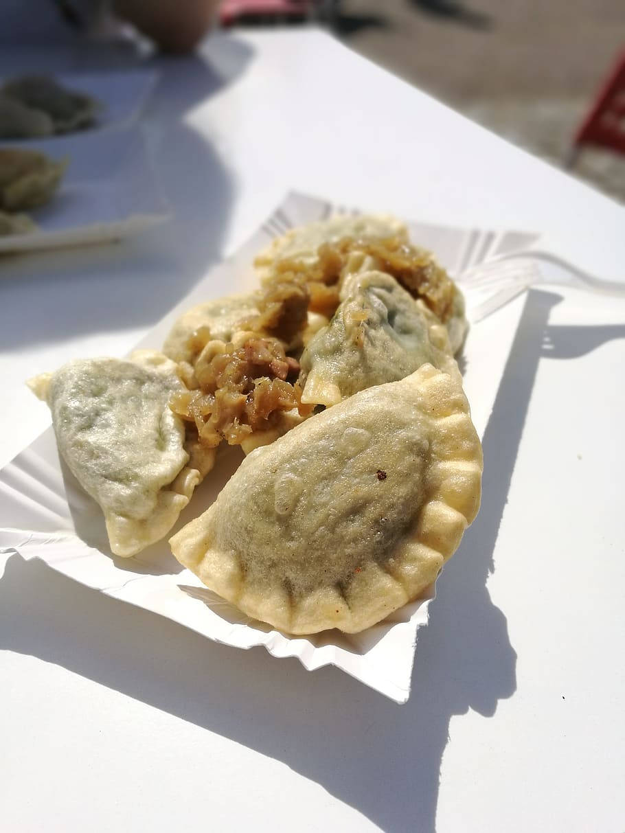 蔬菜餡波蘭餃子 壁紙 — 金黃色的餃子放在白色紙托盤上，在明亮的陽光下投下清晰的陰影。