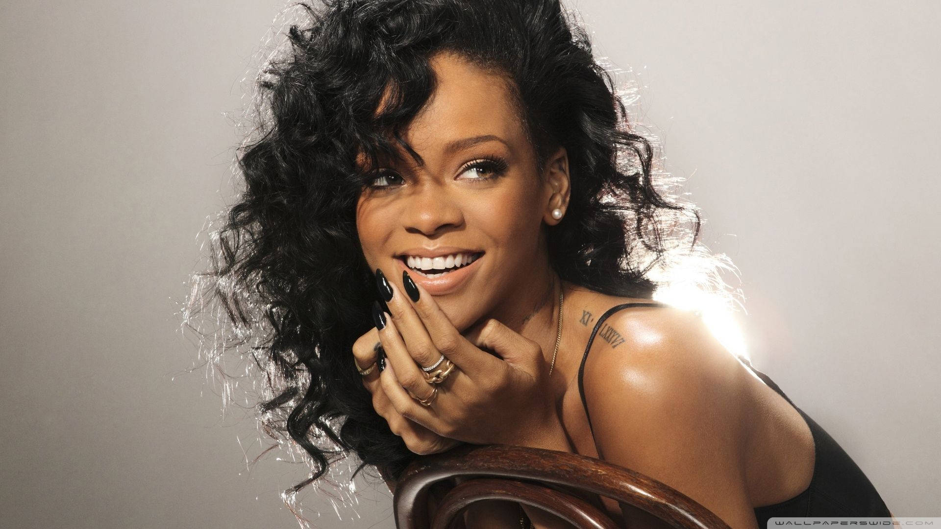 Rihanna 在工作室肖像中微笑，捲髮和綠色指甲。