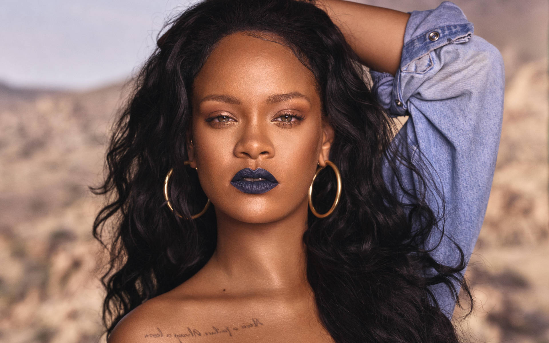 Rihanna 在沙漠環境中塗著深藍色唇膏，戴著金色耳環。