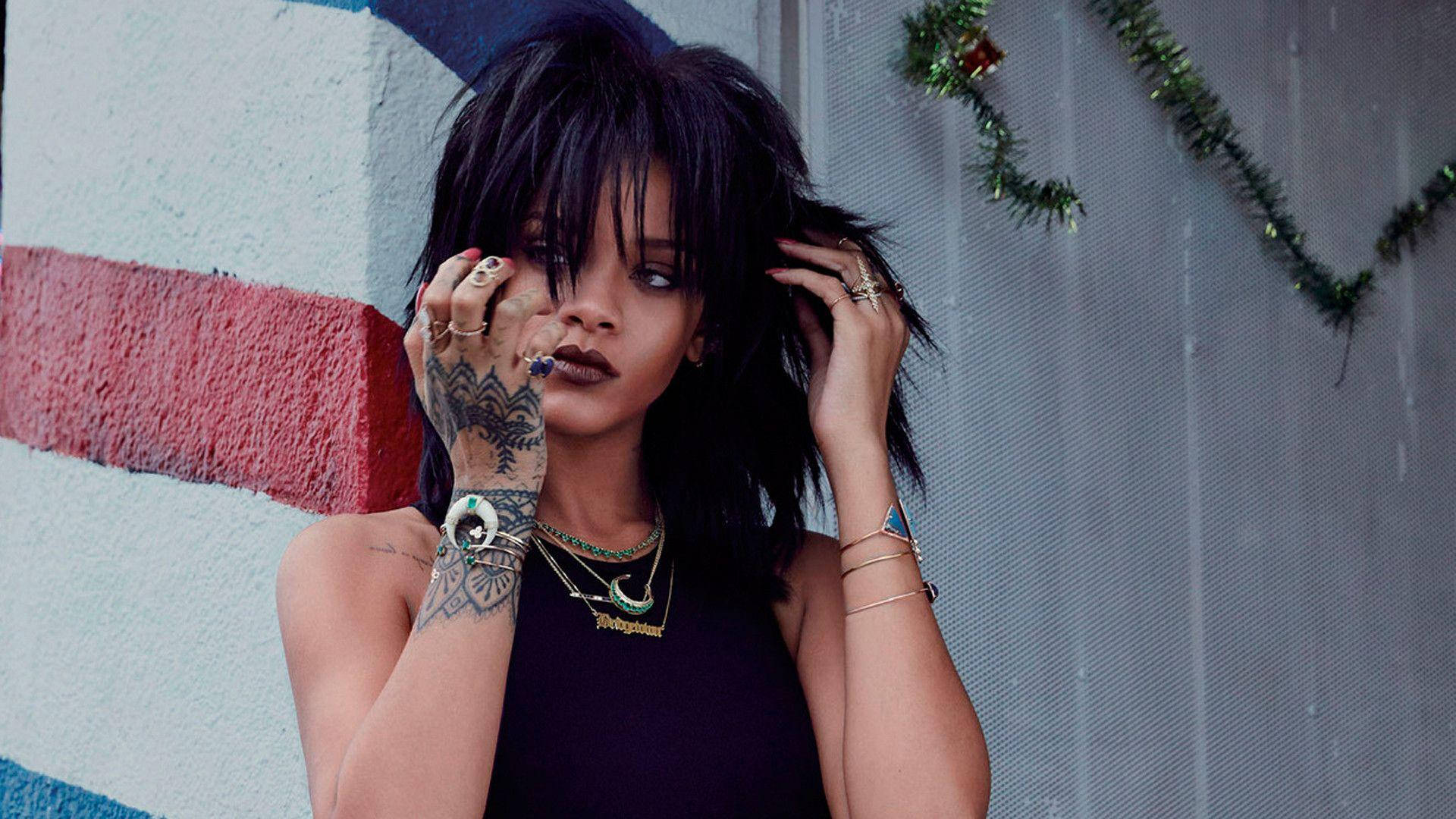 帶有紋身和珠寶的 Rihanna 站在條紋牆壁和節日花環前。