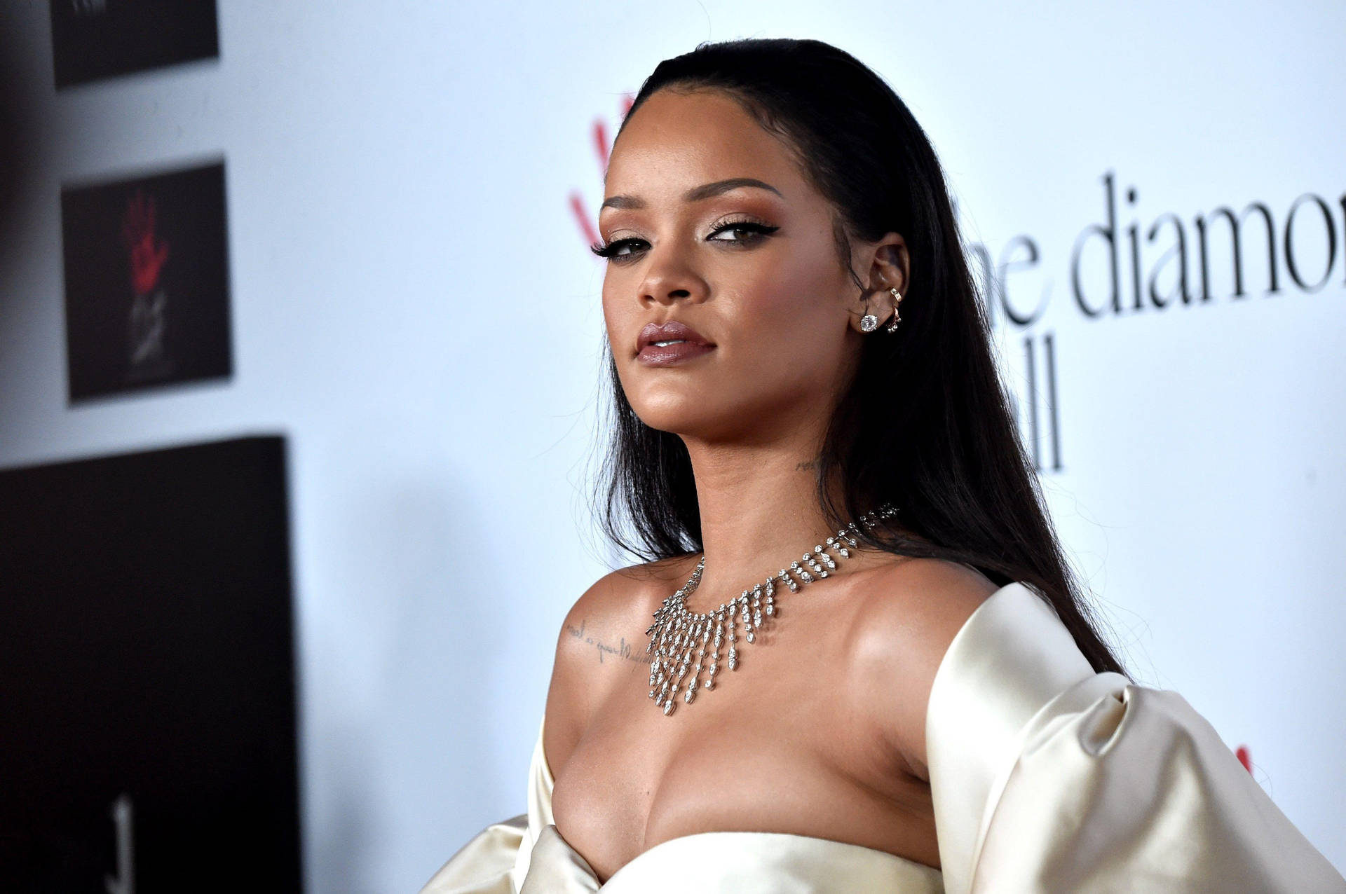 Rihanna 在正式活動中身穿奶油色緞面禮服，佩戴鑽石項鍊。