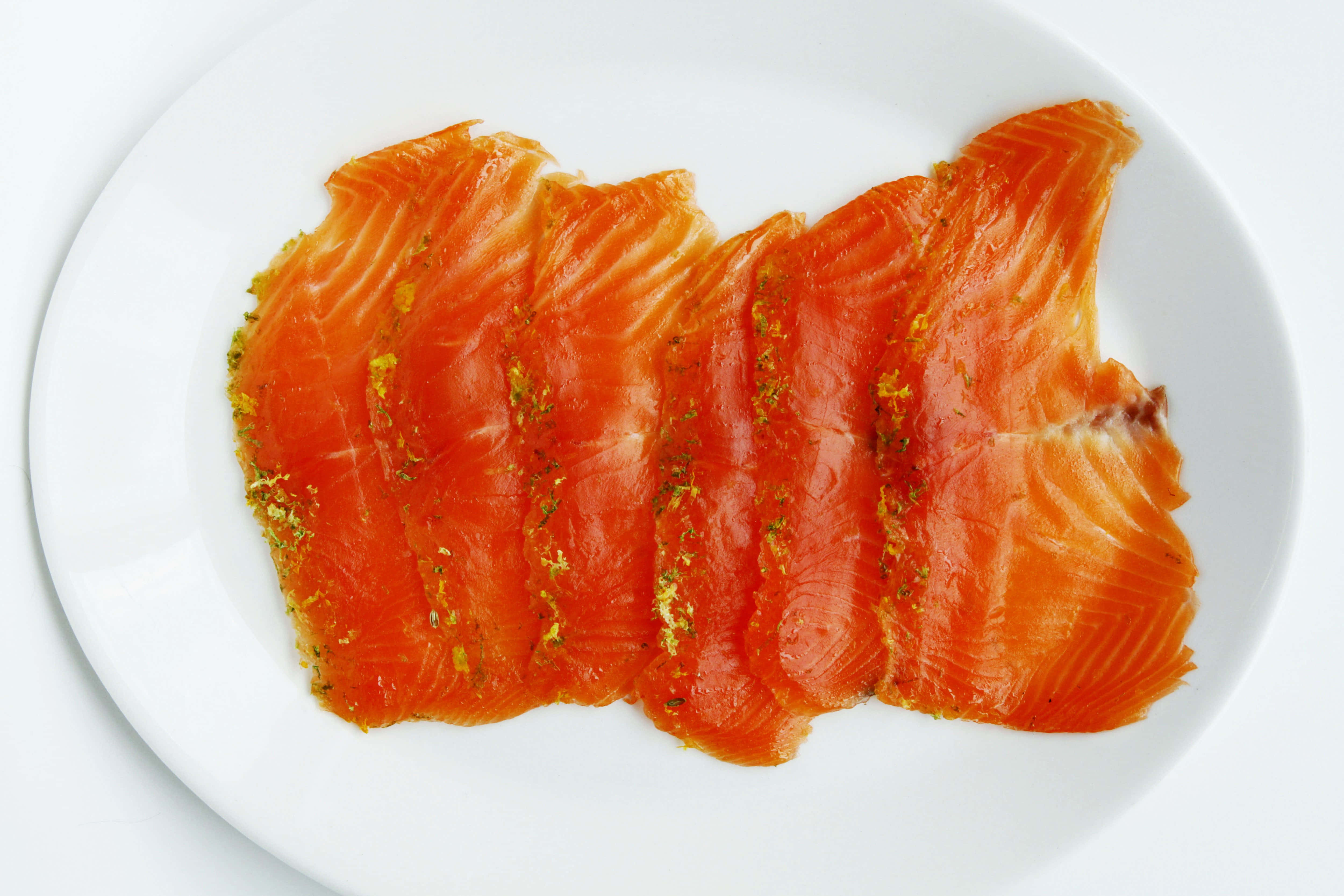 Salmon 桌布 壁紙 — 薄切鮮橙色三文魚，配上金色香草裝飾，藝術地擺放在純白碟上。