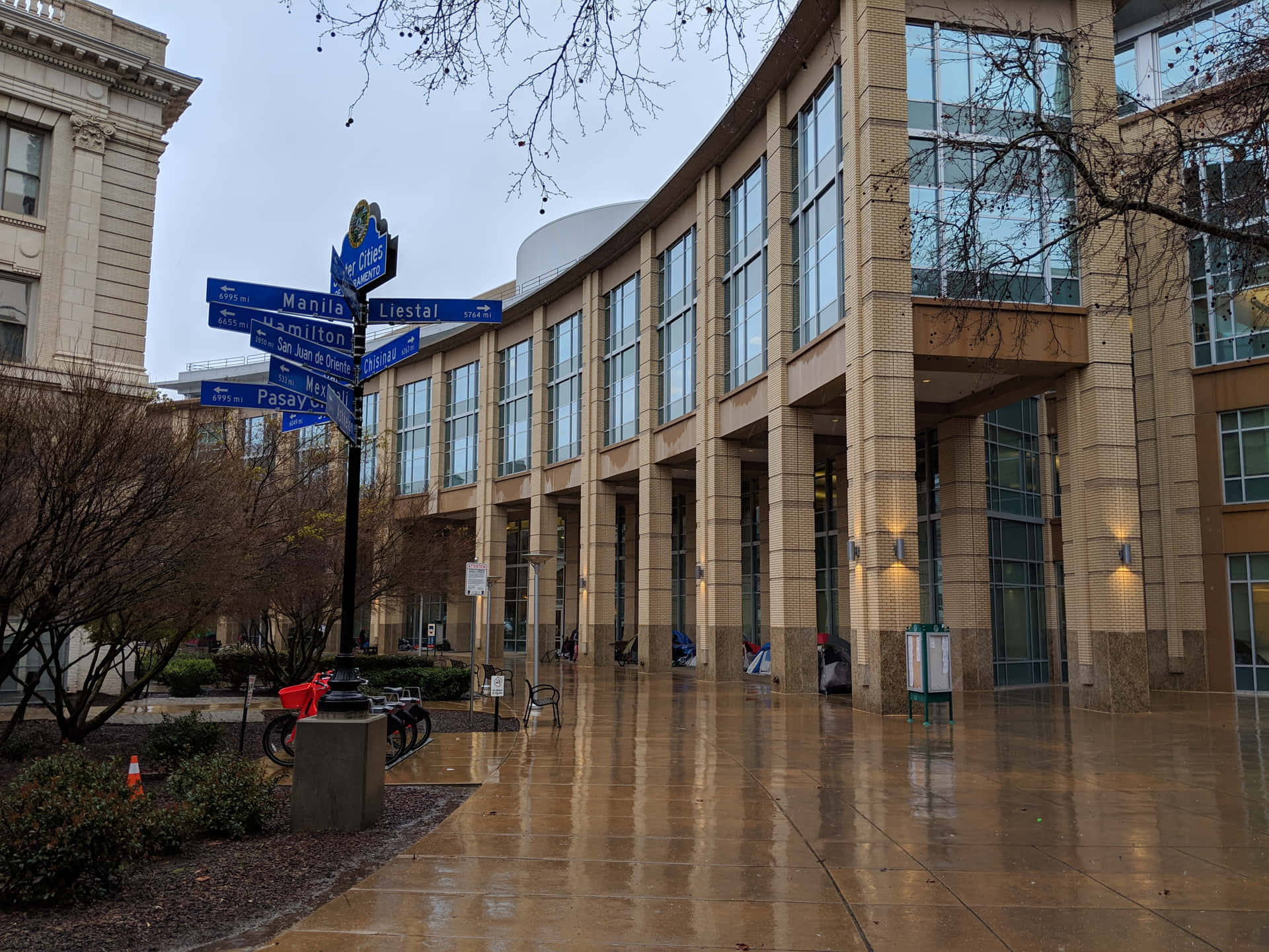 陰天下，濕漉漉的城市廣場，有現代建築和路牌。