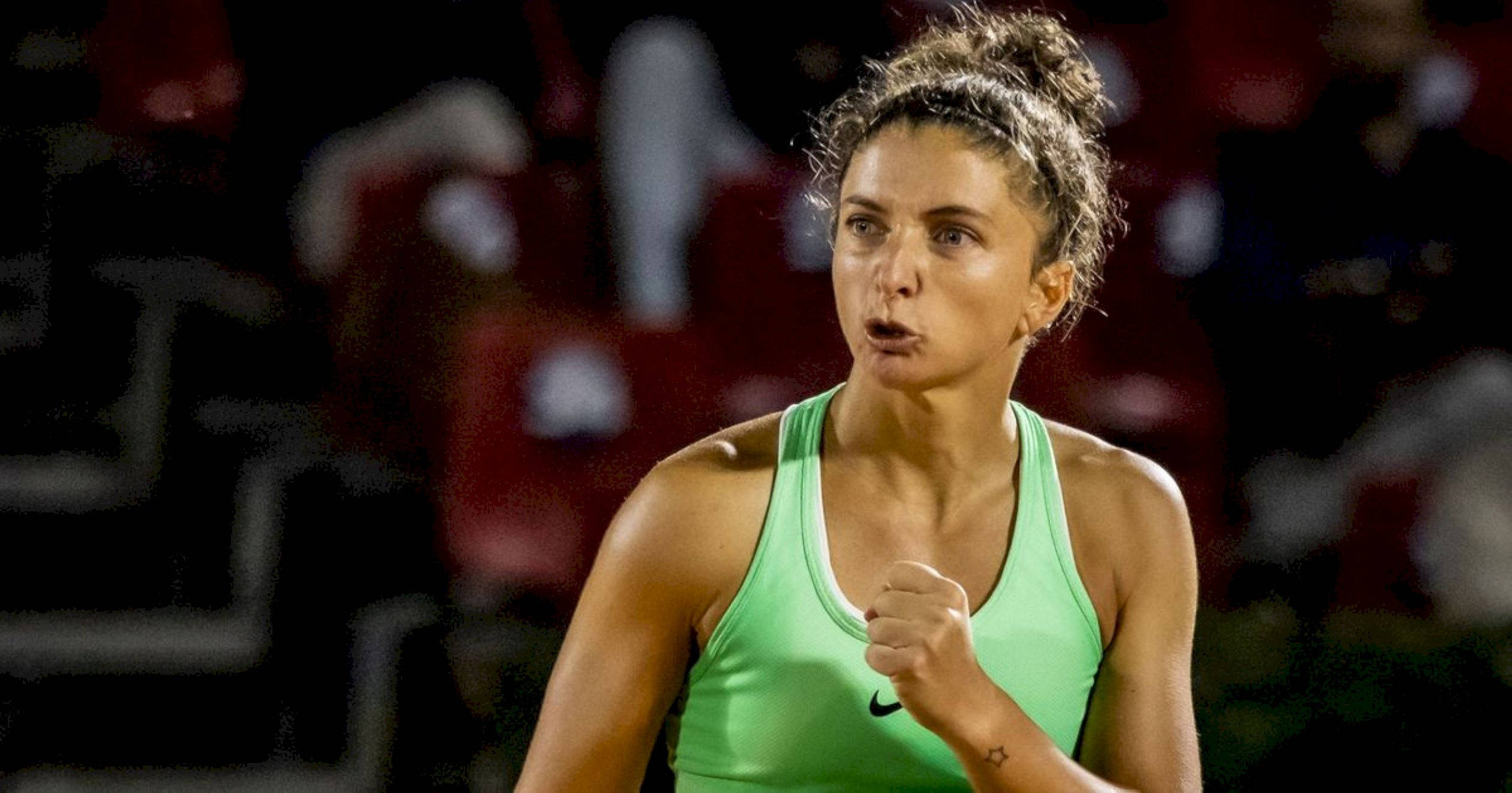 薩拉·埃拉尼堅定握拳 壁紙 — 一位專注的女網球運動員穿著亮綠色上衣，在球場燈光下比賽中握緊拳頭。