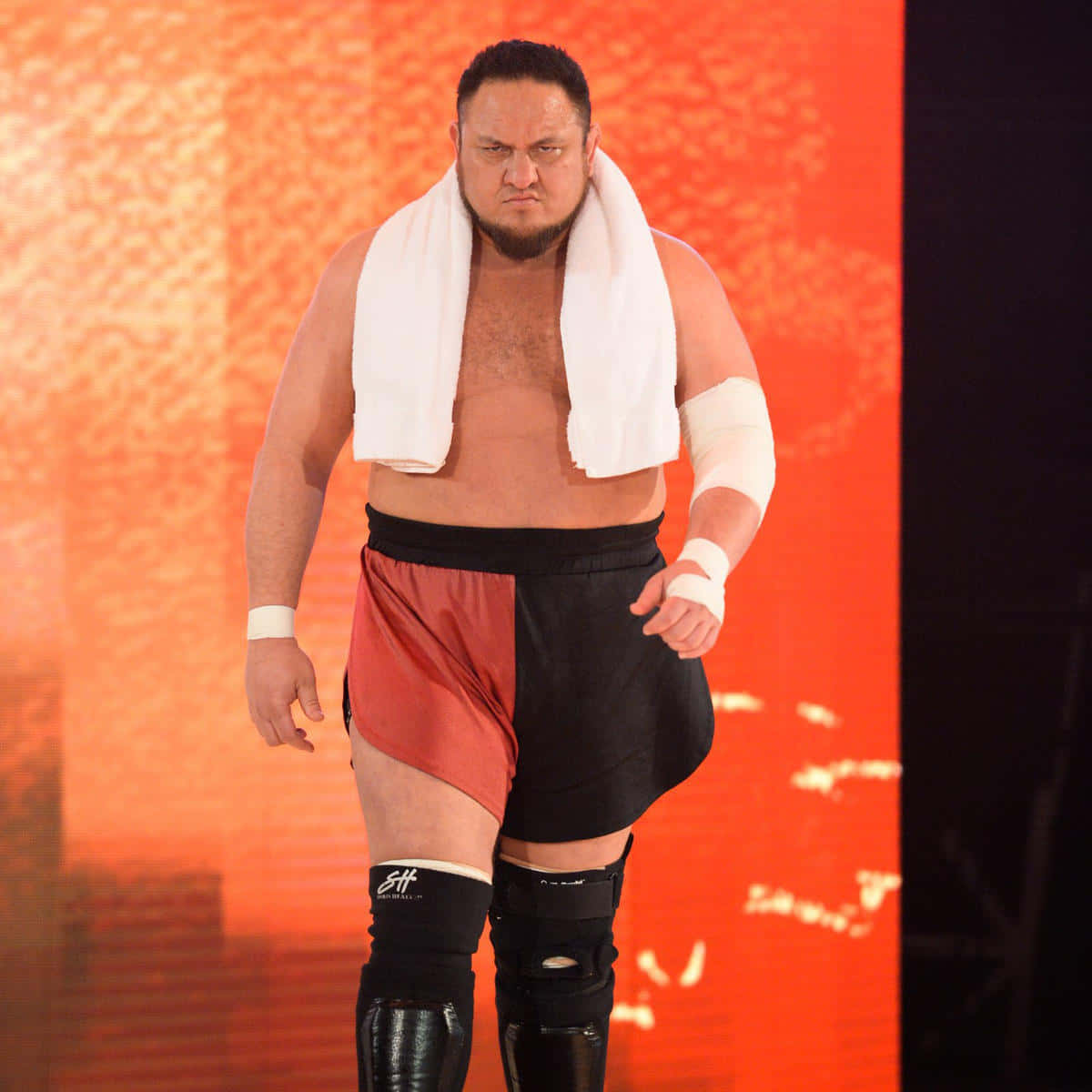 薩摩亞·喬WWE RAW主賽事準備出戰 壁紙 — 一個肌肉發達的摔角手，肩上披著白色毛巾，在發光的橙色背景下帶著兇猛的表情向前邁進。