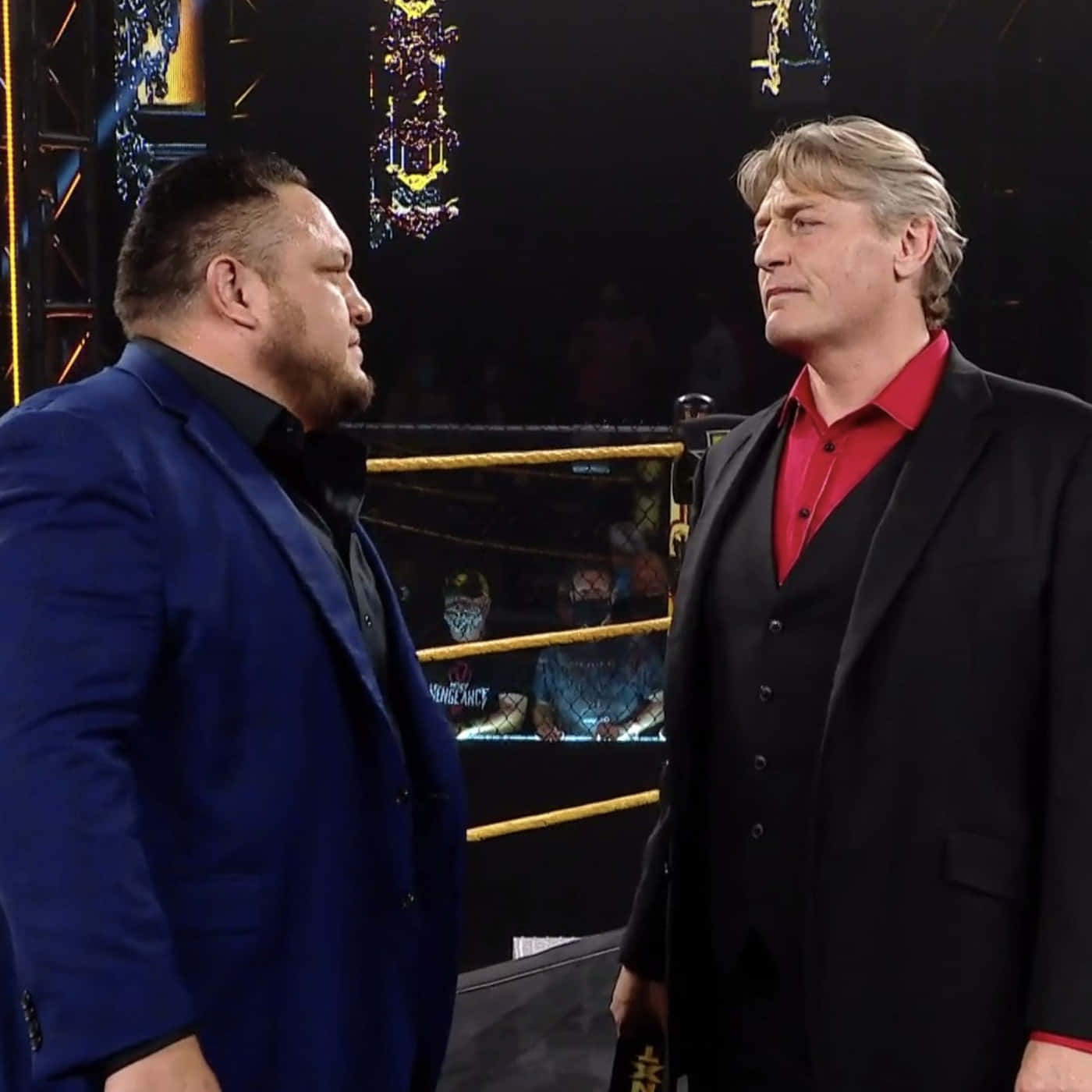 薩摩亞·喬在WWE NXT賽事中展現壓迫性眼神 壁紙 — 兩名身穿西裝的男子在摔角擂台上對峙，上方有華麗裝飾，舞台燈光明亮。