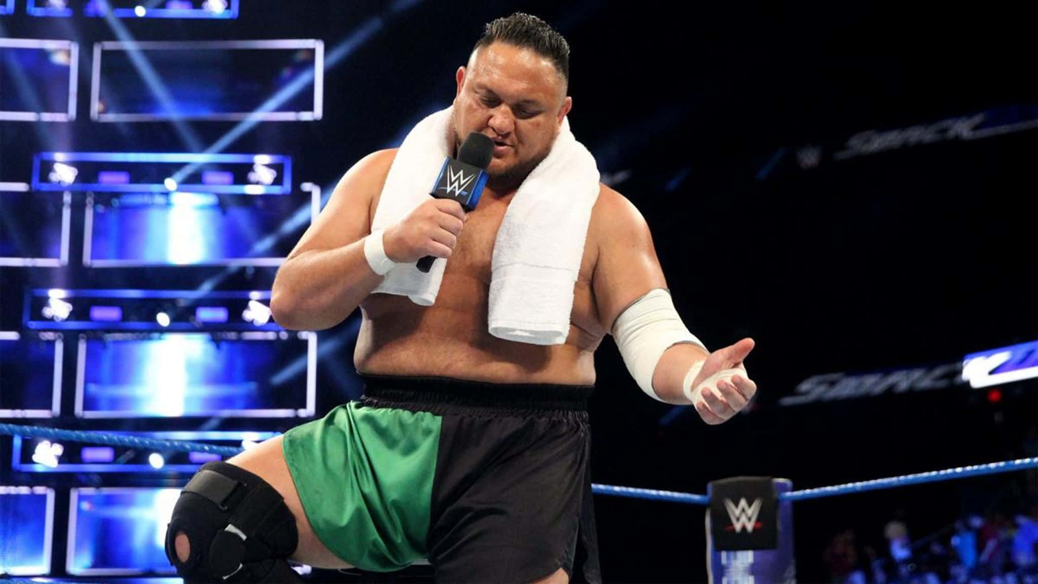 薩摩亞·喬於WWE SmackDown賽事中麥克風辱罵 壁紙 — WWE摔角手肩上搭著毛巾，在燈光明亮的擂台內對著麥克風說話。