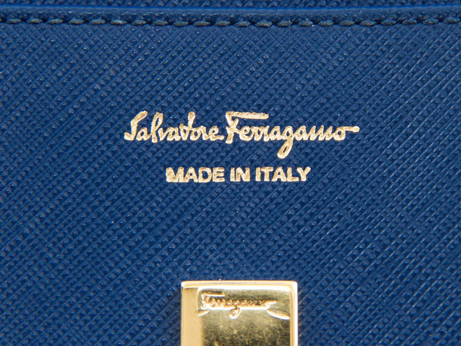 薩爾瓦托·菲拉格慕「義大利製造」 壁紙 — Salvatore Ferragamo 皇家藍色紋理皮革銀包特寫，帶有金色箔標誌和金屬扣。