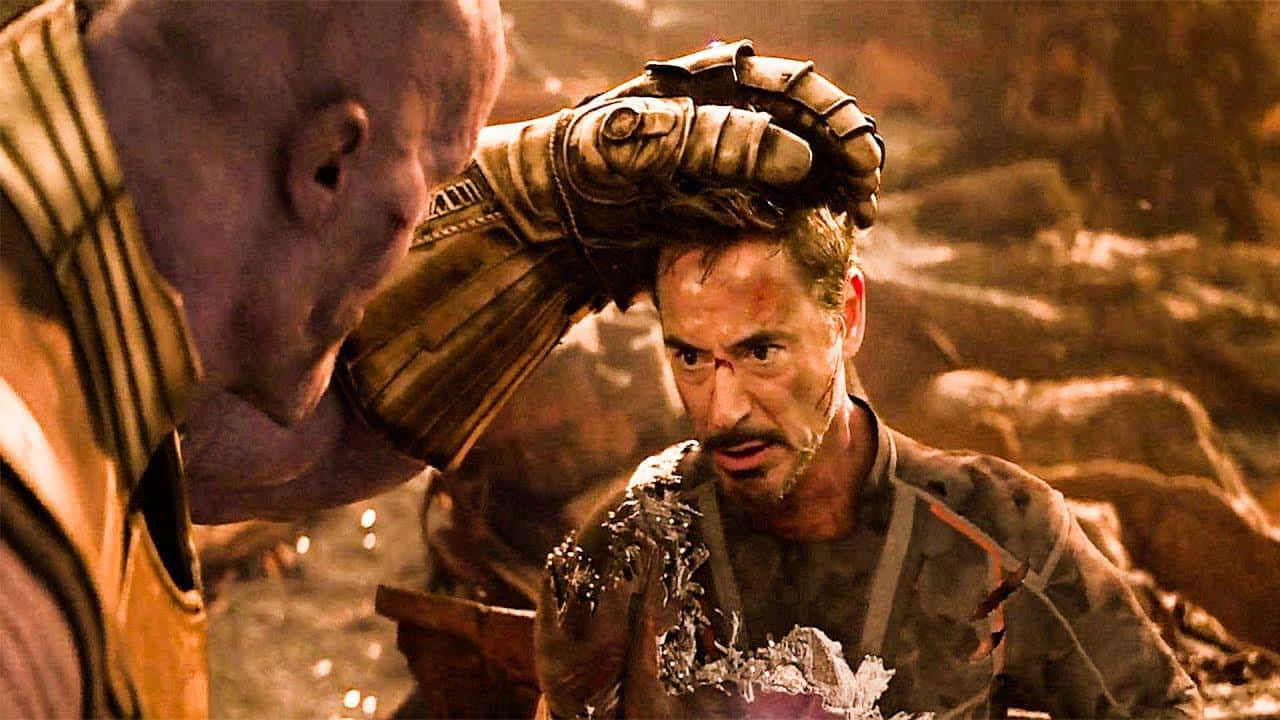 Iron Man And Thanos 桌布 壁紙 — 薩諾斯在瓦礫和熾熱的橙色光芒中，抓住鐵甲奇俠的頭部，形成一個戲劇性的電影時刻。