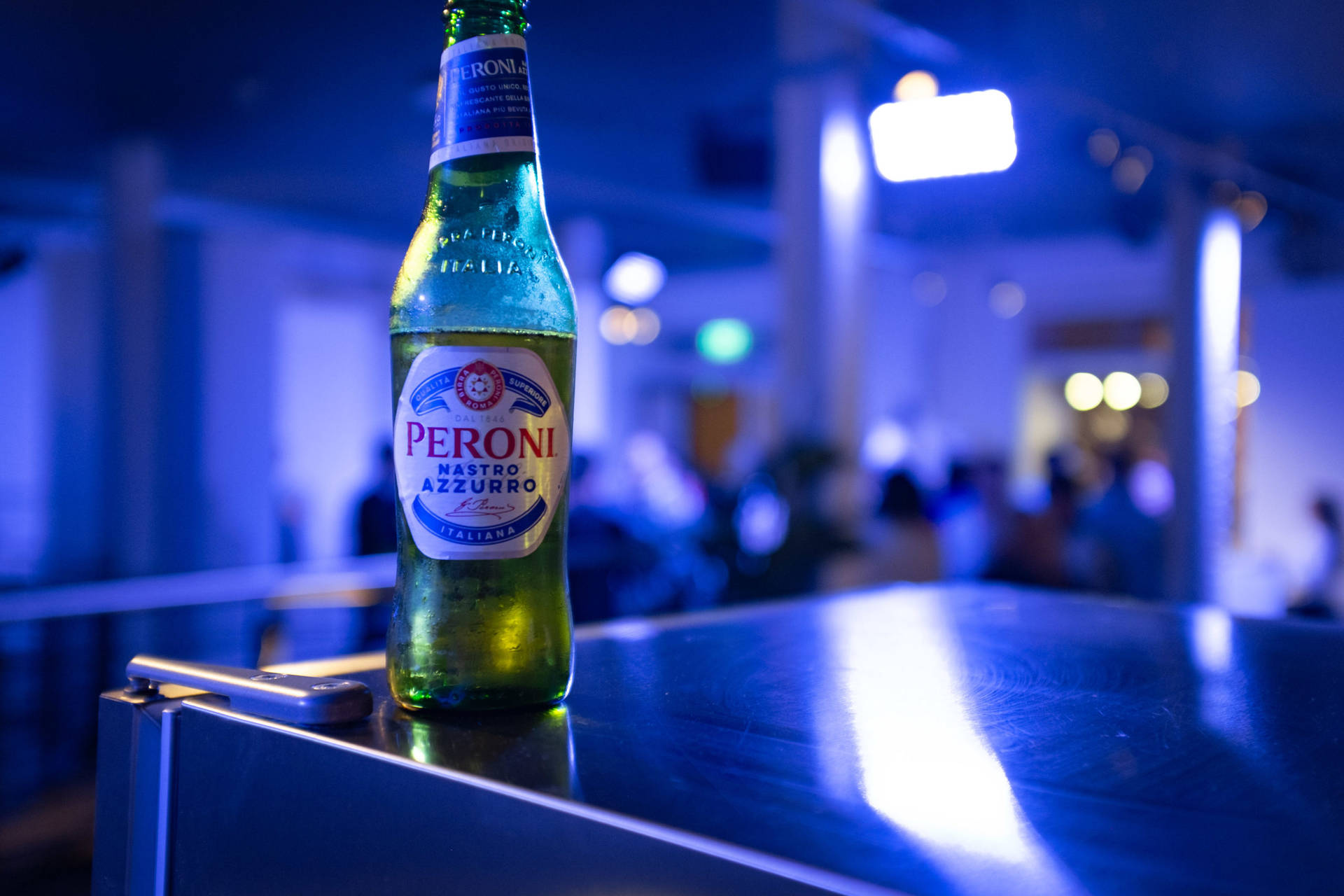 在藍色燈光的夜生活環境中，吧檯上的一瓶冰凍Peroni啤酒。