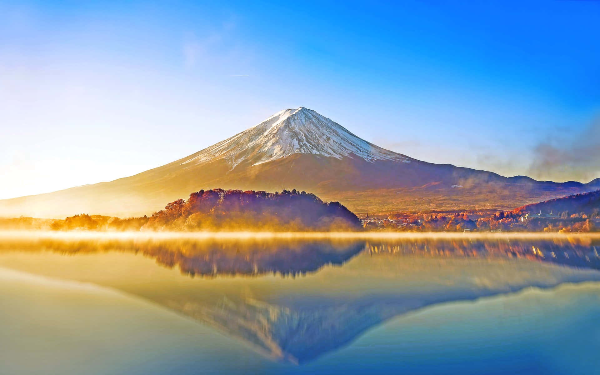 富士山倒映在霧氣繚繞的湖面上，日出時分金色光芒。
