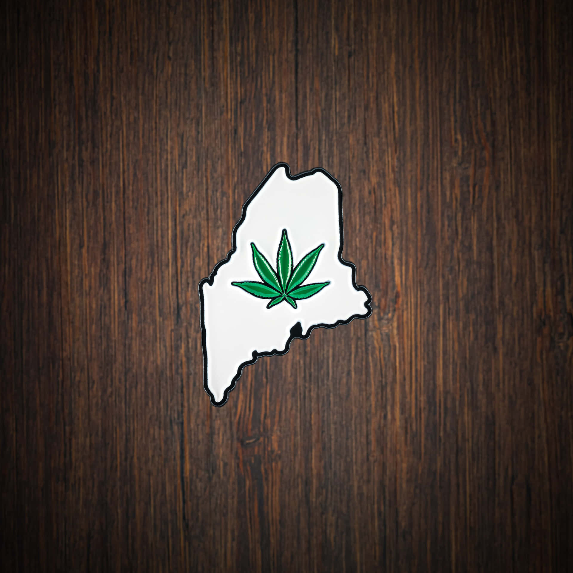 白色麻薩諸塞州輪廓別針，帶有綠色大麻葉，置於深色木上。