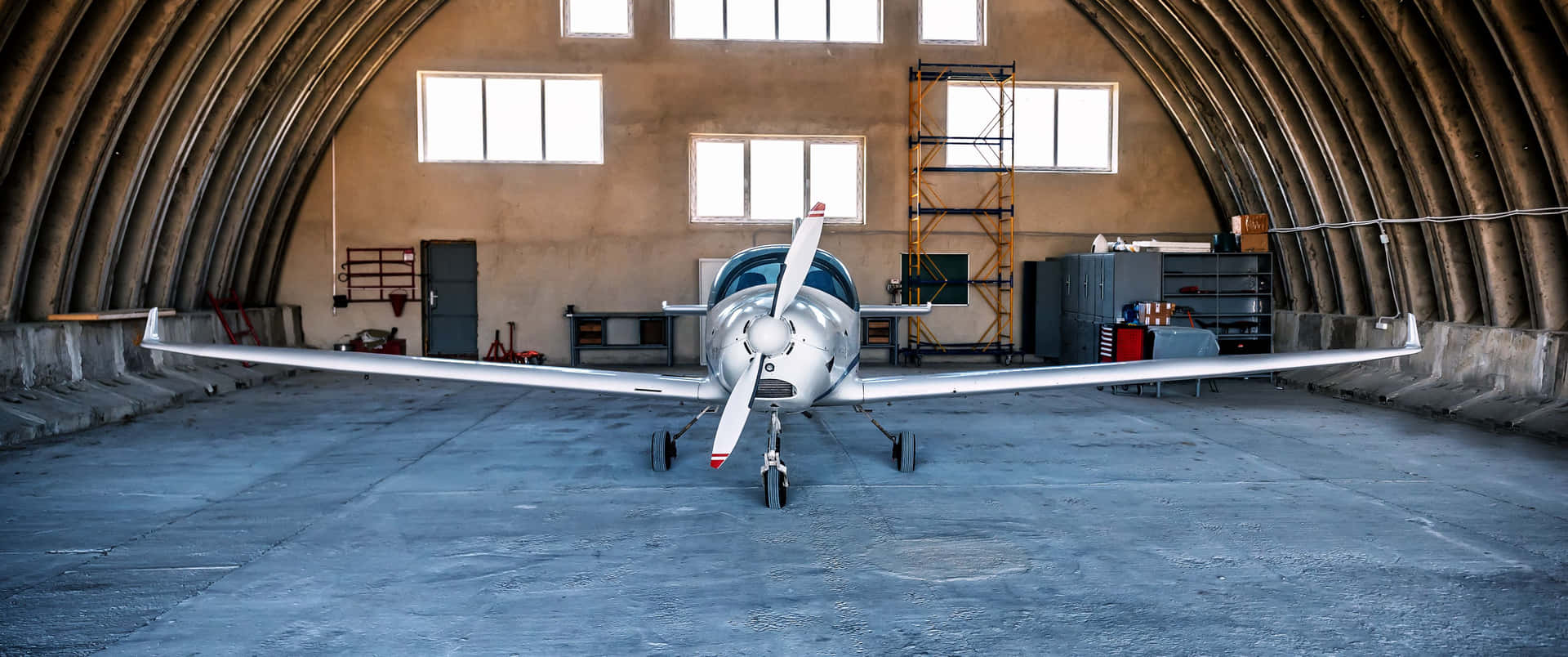 銀色飛機停放在大型拱形機庫內，有混凝土地板和窗戶。