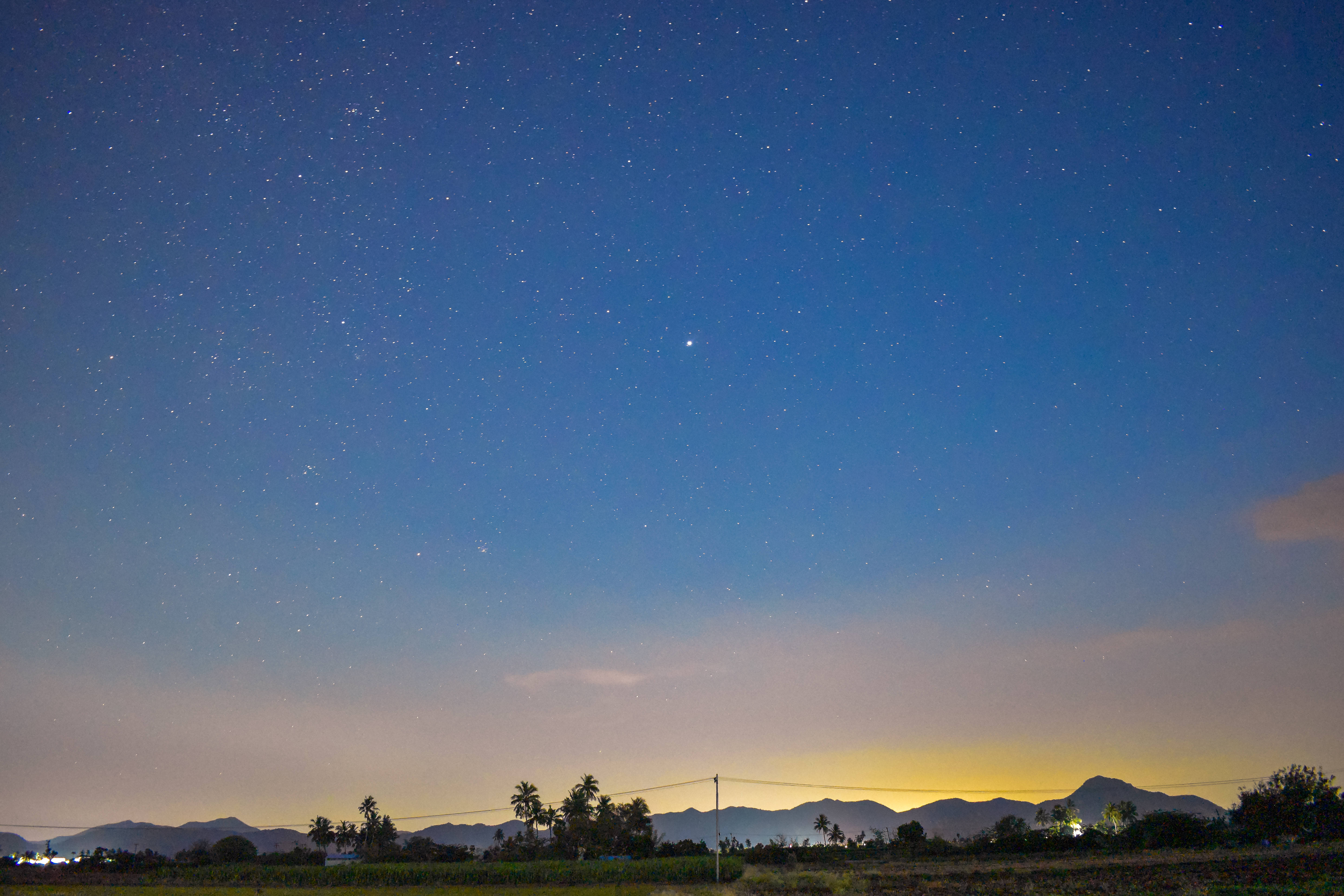 藍天最佳桌面 壁紙 — 繁星點點的夜空拱起在遠山和剪影般的鄉村景觀之上，閃爍著暮色的色調。
