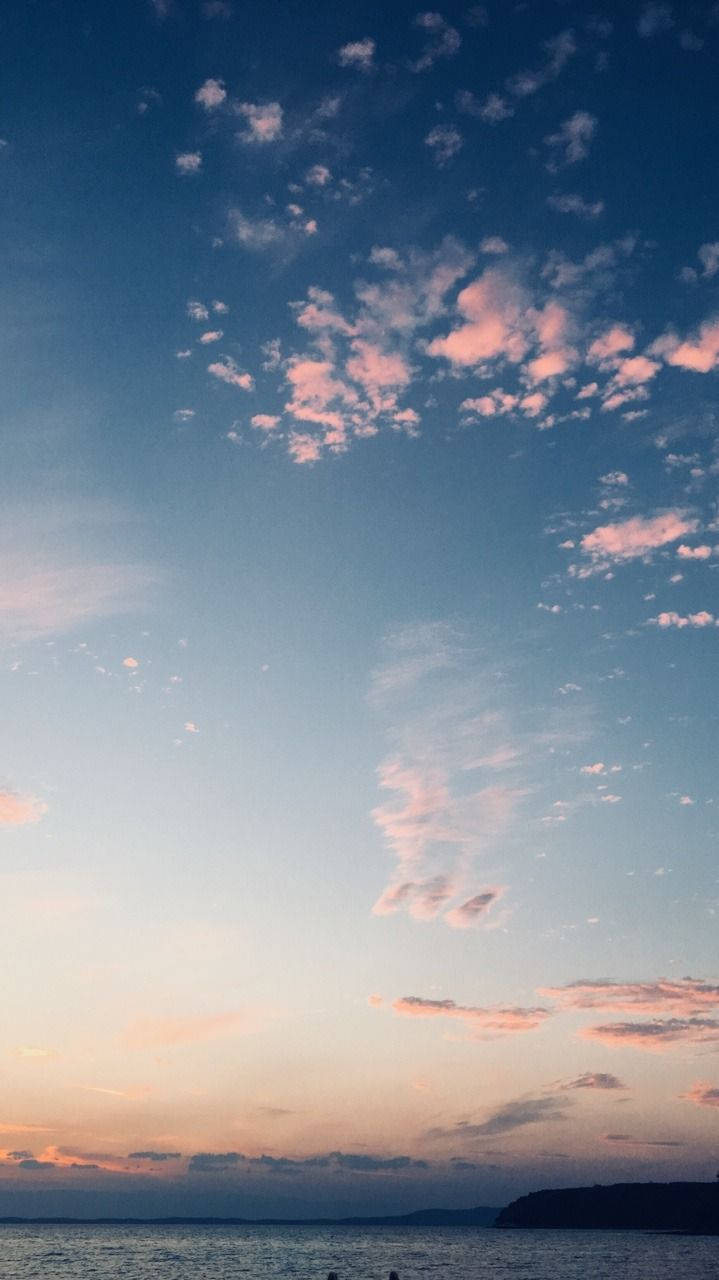 日落時分，平靜的水面和遠處陸地上空的粉紅色和藍色雲彩。