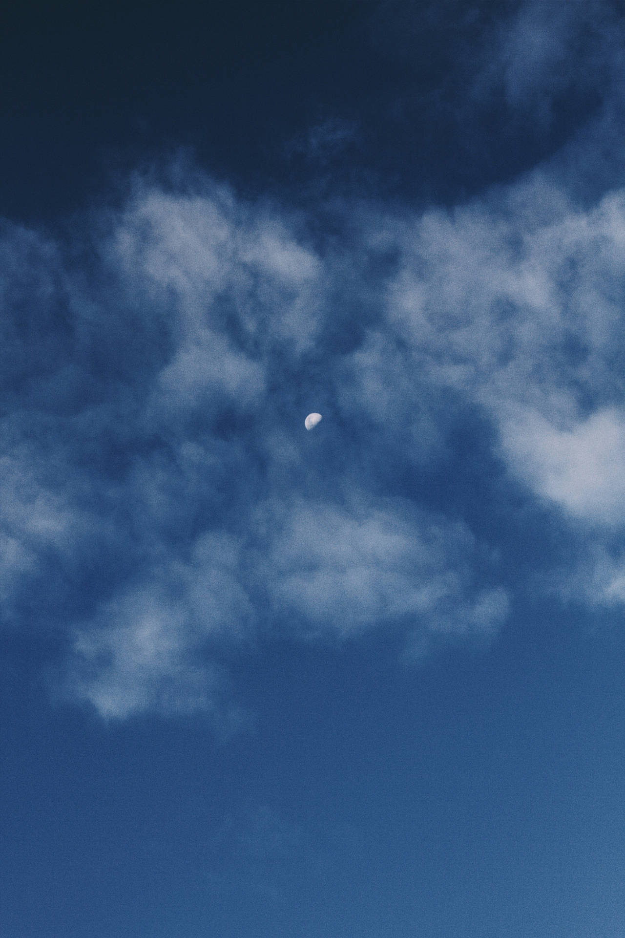 在深藍色的夜空中，透過柔軟的雲層可見的月牙。