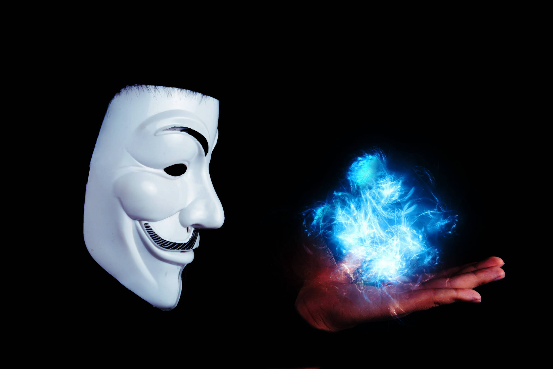 白色 Guy Fawkes 面具看著黑色背景中手中的藍色發光能量球