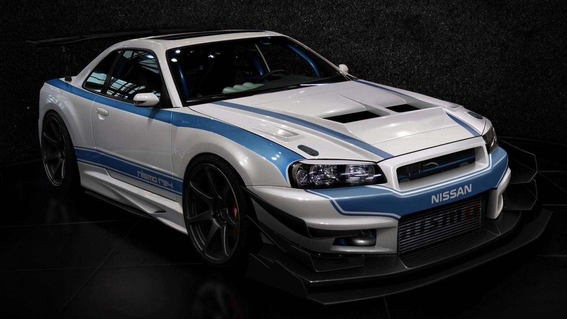 藍白相間的尼桑Skyline汽車 壁紙 — 一輛白色和藍色的日產Skyline GT-R R34，帶有賽車條紋和黑色輪圈，在工作室燈光下展示在深色紋理背景前。