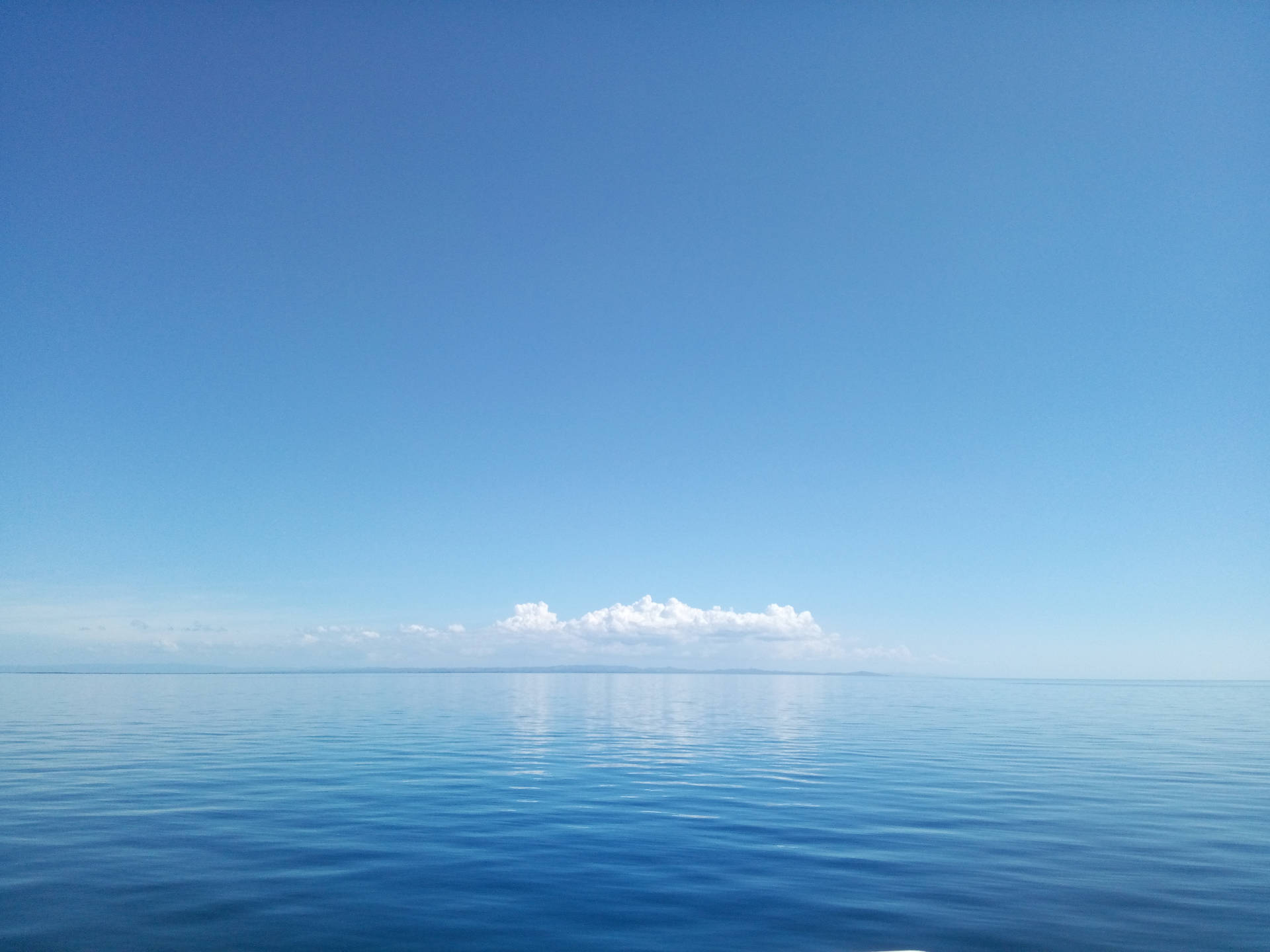 平靜的海洋反射著地平線上一朵雲的清澈藍天。
