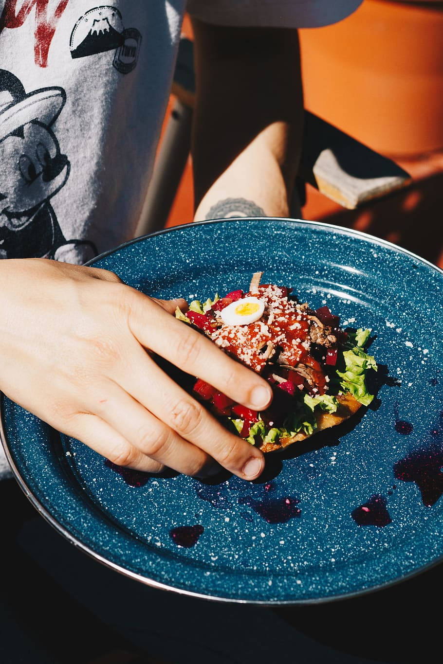 藍盤裝 enchiladas 壁紙 — 一隻手拿著一個色彩繽紛的開放式三文治，上面放有甜菜根藜麥和半個水煮蛋，放在一個有斑點的藍色碟子上。