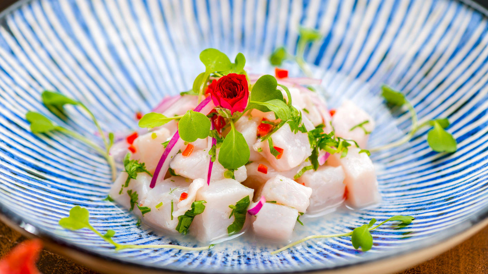 酸橘汁醃魚配魚肉、微型蔬菜和紅色花朵裝飾，盛在藍色條紋碗中。