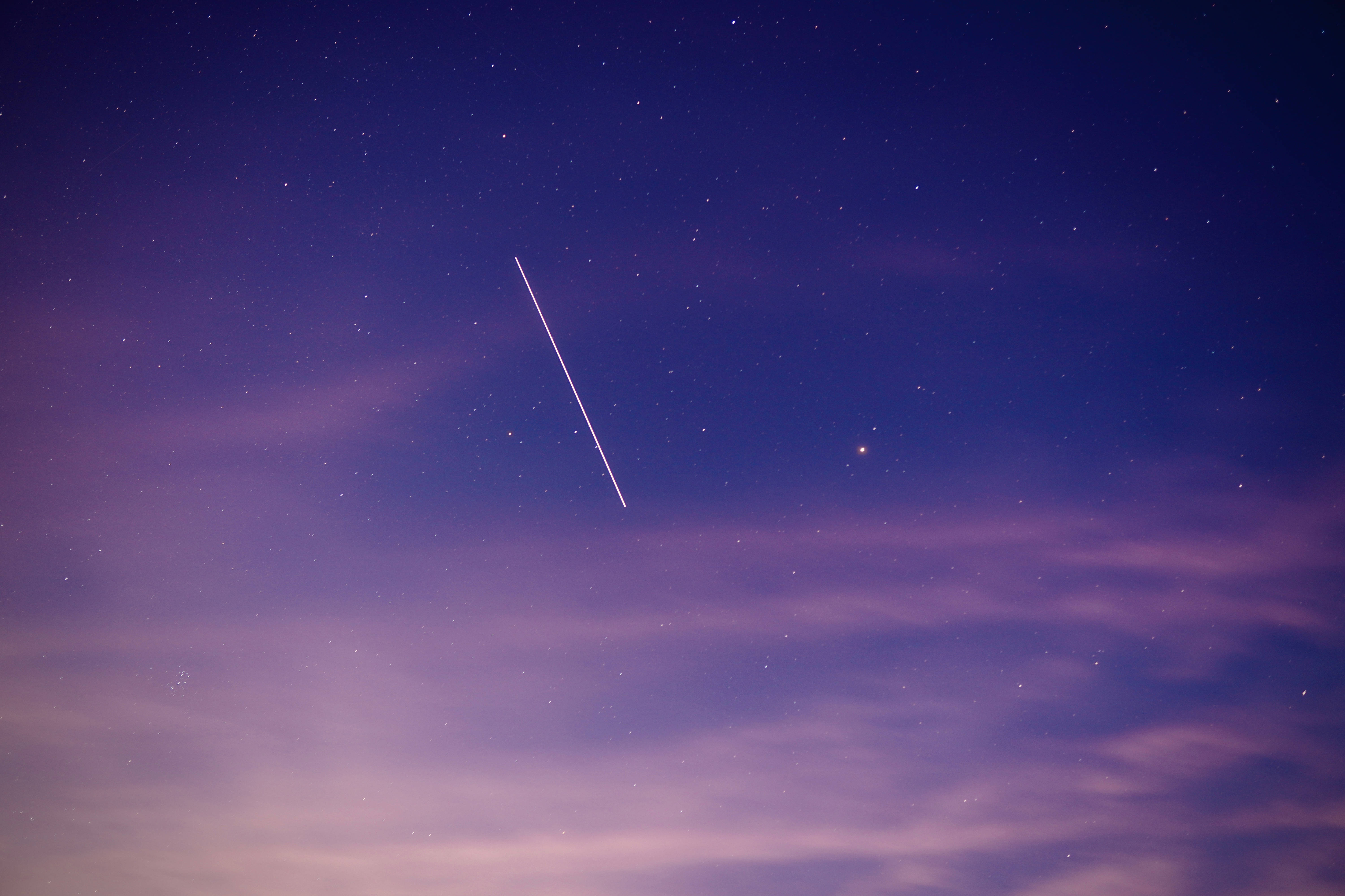 藍紫色星系中的兩顆星星 壁紙 — 一顆明亮的流星斜斜劃過深紫和藍色調的星空暮色天空。