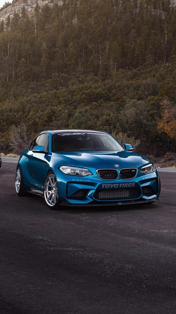 藍色BMW M2跑車停在森林道路上，背景有樹木。