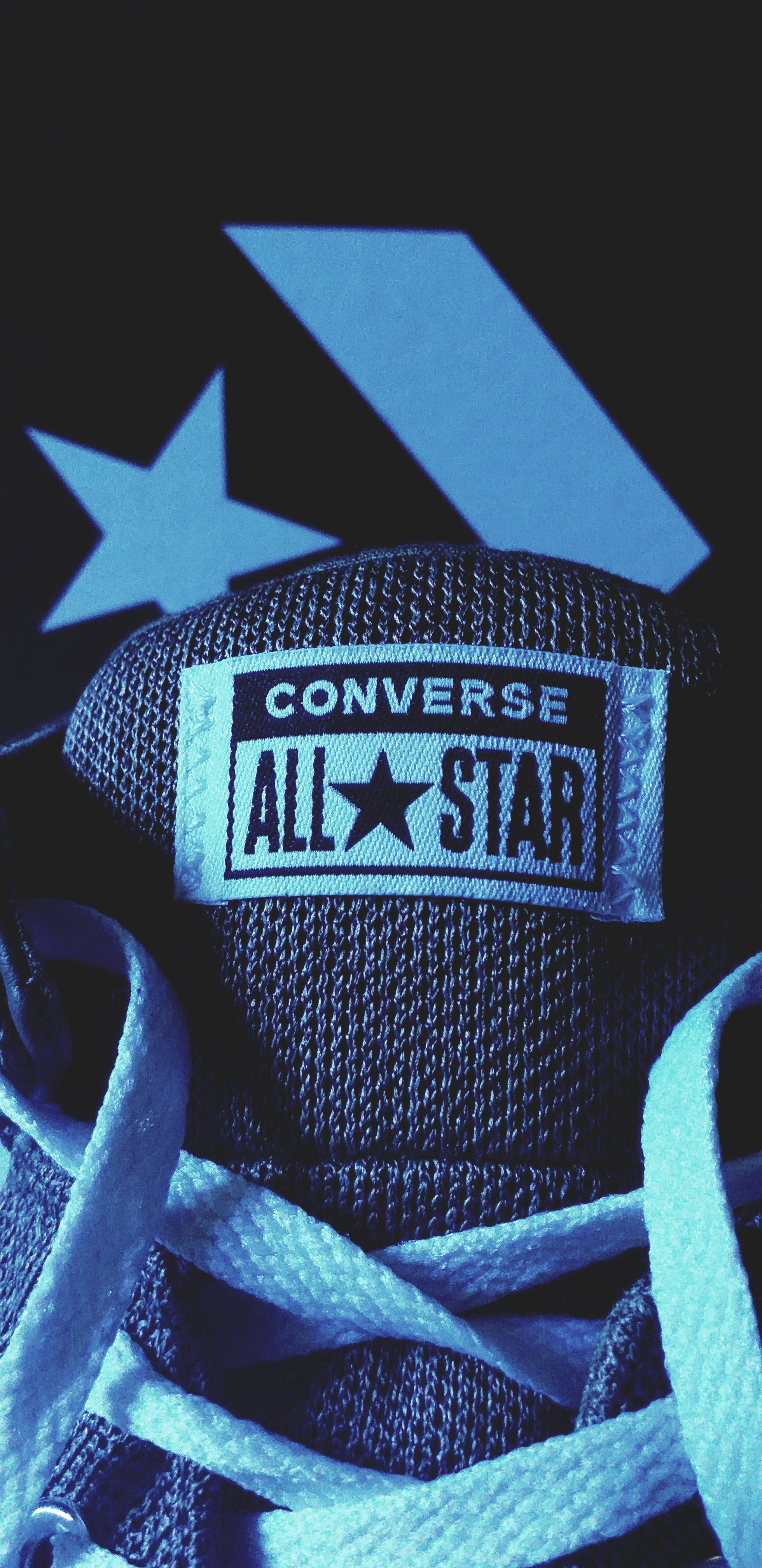 藍色All-Star Converse標誌 壁紙 — 藍色調的 Converse All Star 運動鞋特寫，帶有標誌和鞋帶，背景為深色，帶有星星和 V 形圖案。